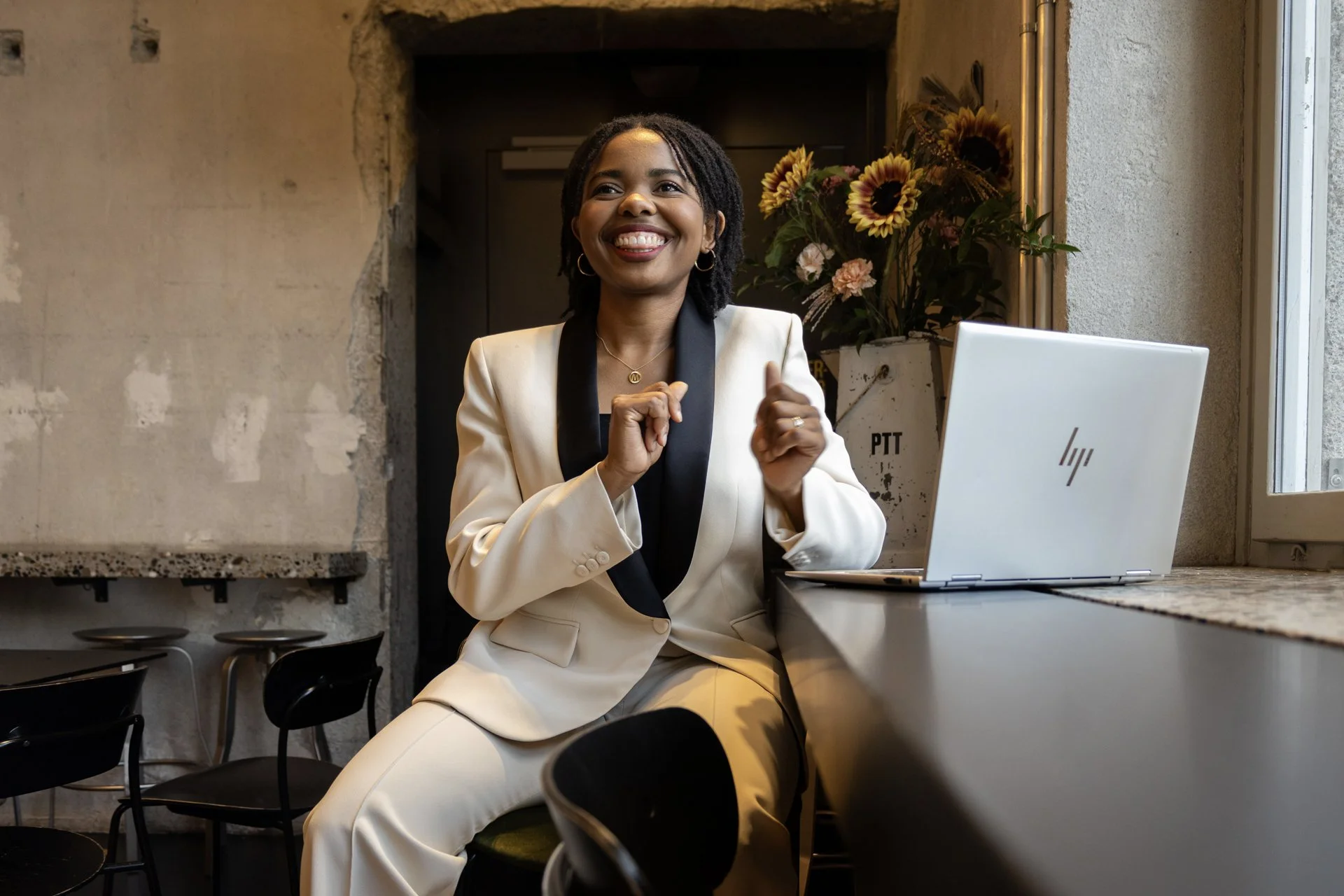 Maphrida Wehrli smiling woman in a cream-colored suit sitting on a stool at a kitchen counter with a laptop, looking happy and relaxed.
