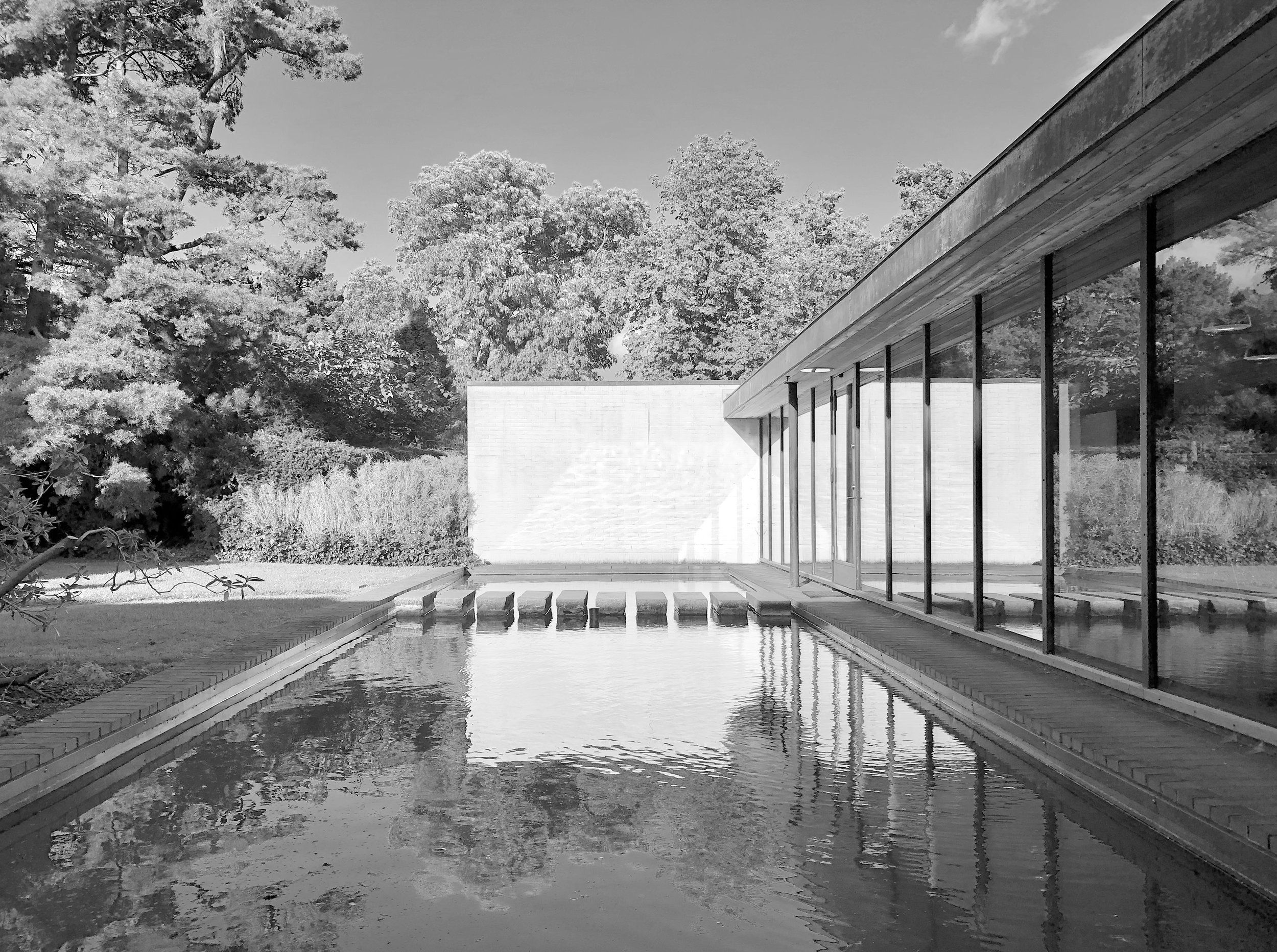 Schlichte moderne Hausarchitektur mit großem Fenster, Blick auf Wasserstrahl und Natur im Hintergrund, schwarz-weiß Foto.
