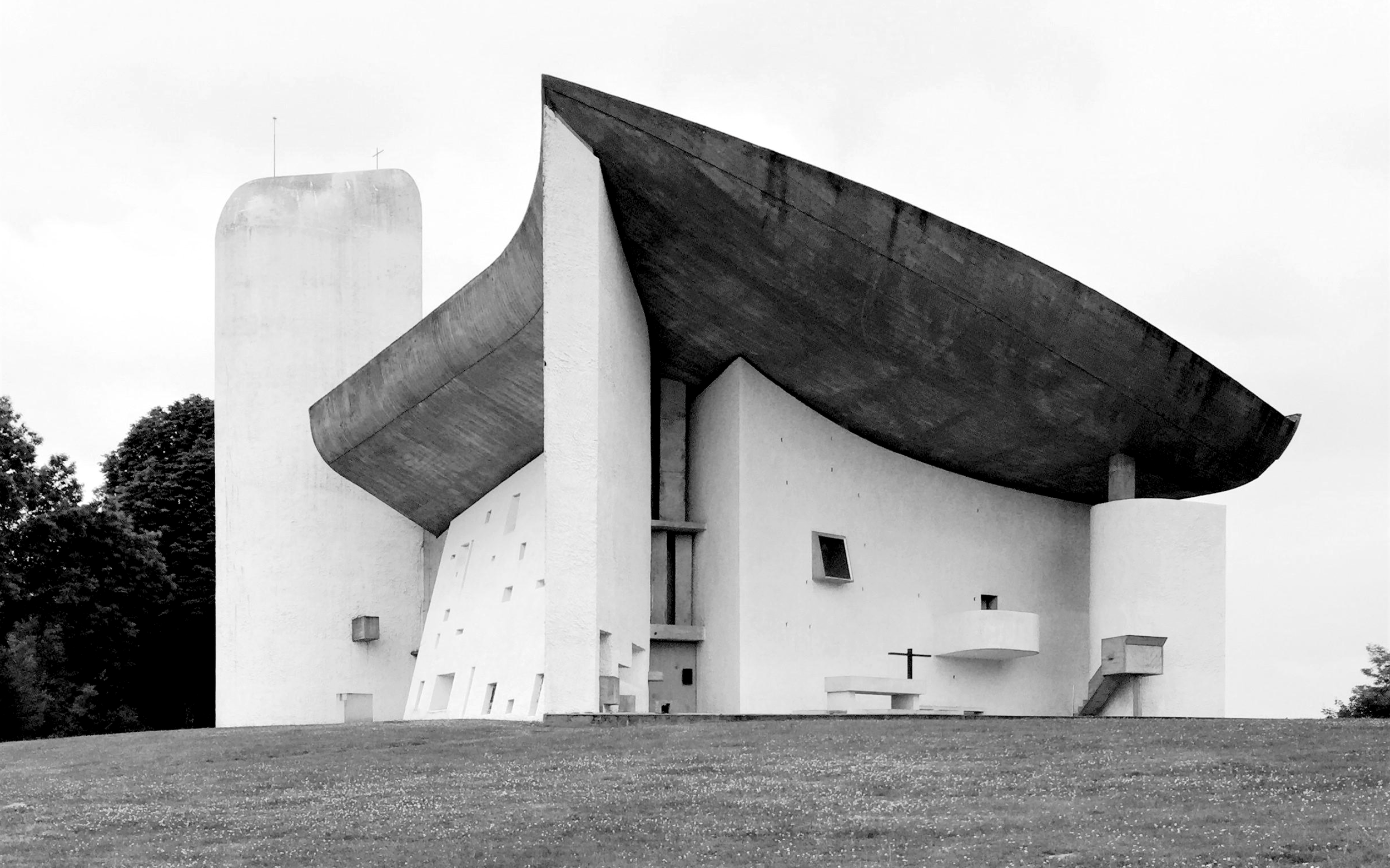 Schwarze und weiße Aufnahme eines modernen, ungewöhnlich gestalteten Kirchengebäudes mit großen schmetterlingsförmigen Dächern und weißen Wänden.