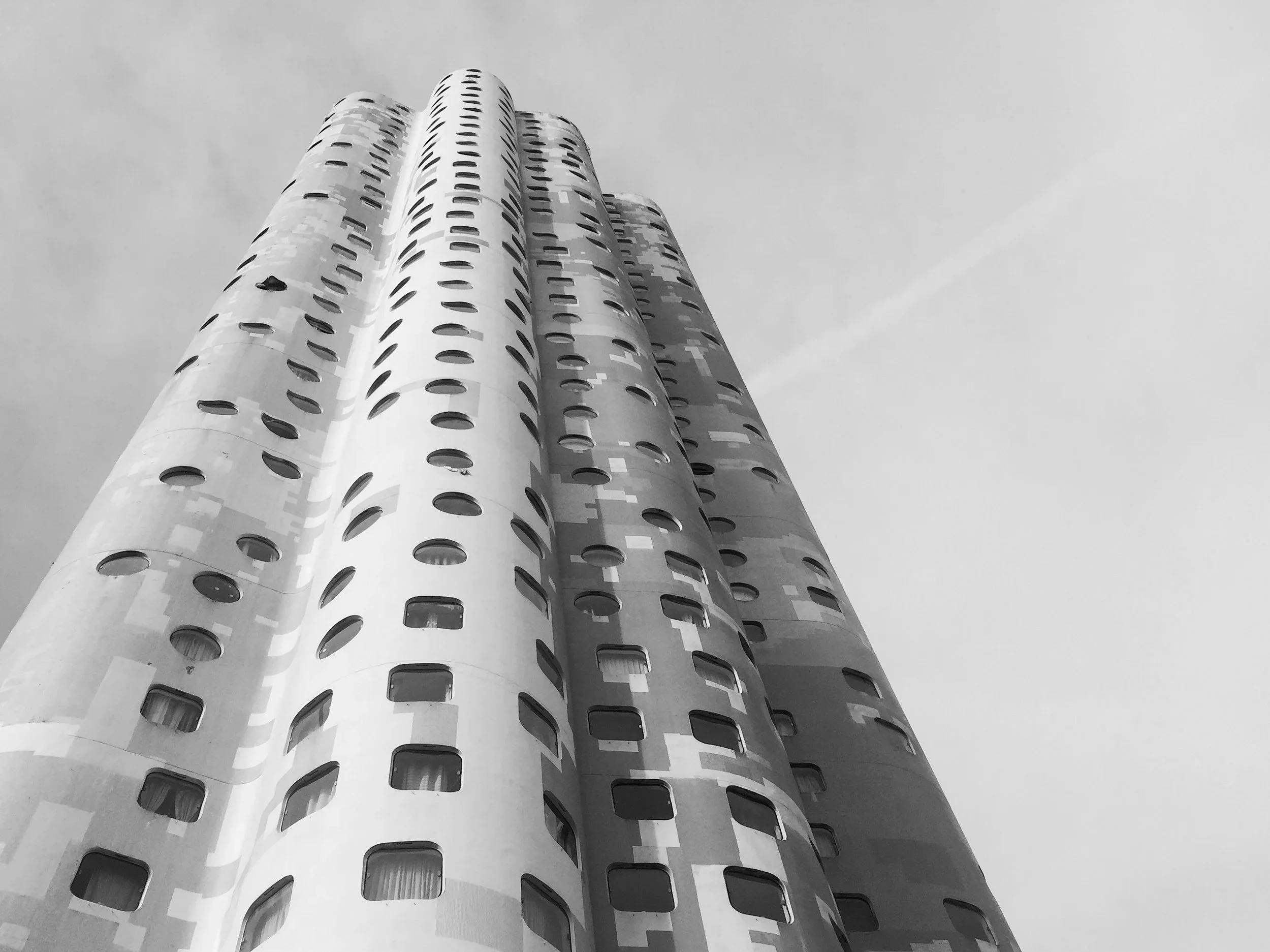 Schwarz-Weiß-Foto eines modernen Wolkenkratzers mit runden Fenstern, aufgenommen aus niedriger Perspektive, Blick nach oben