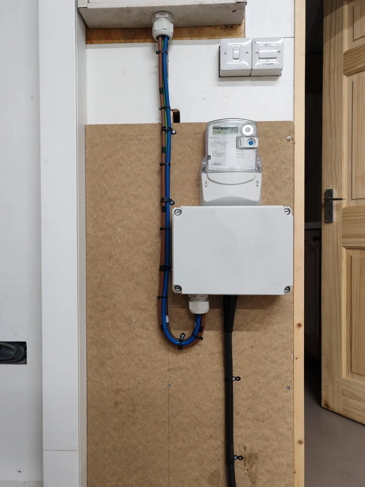Electrical meter and plumbing pipes installed on wooden board in utility room.