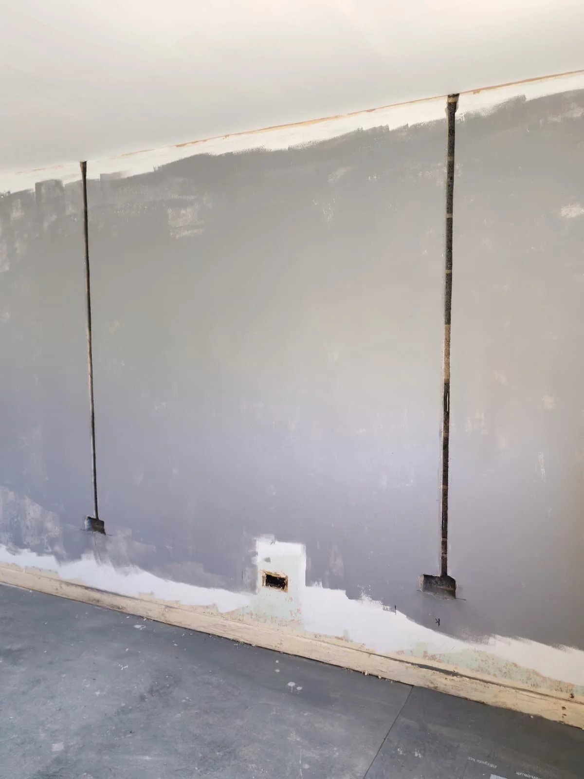 This image shows a room wall with electrical wiring and outlets exposed, and unfinished drywall surface with patches of primer or paint.