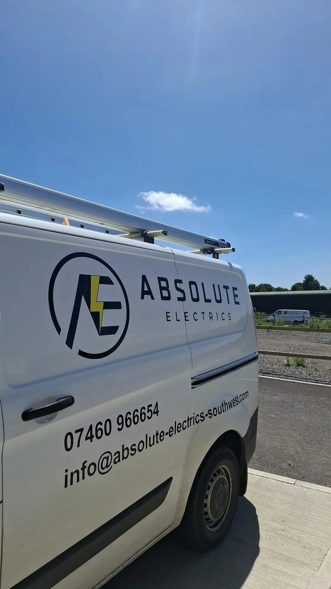 A white van with the logo and contact information for Absolute Electrics parked outdoors on a bright sunny day.