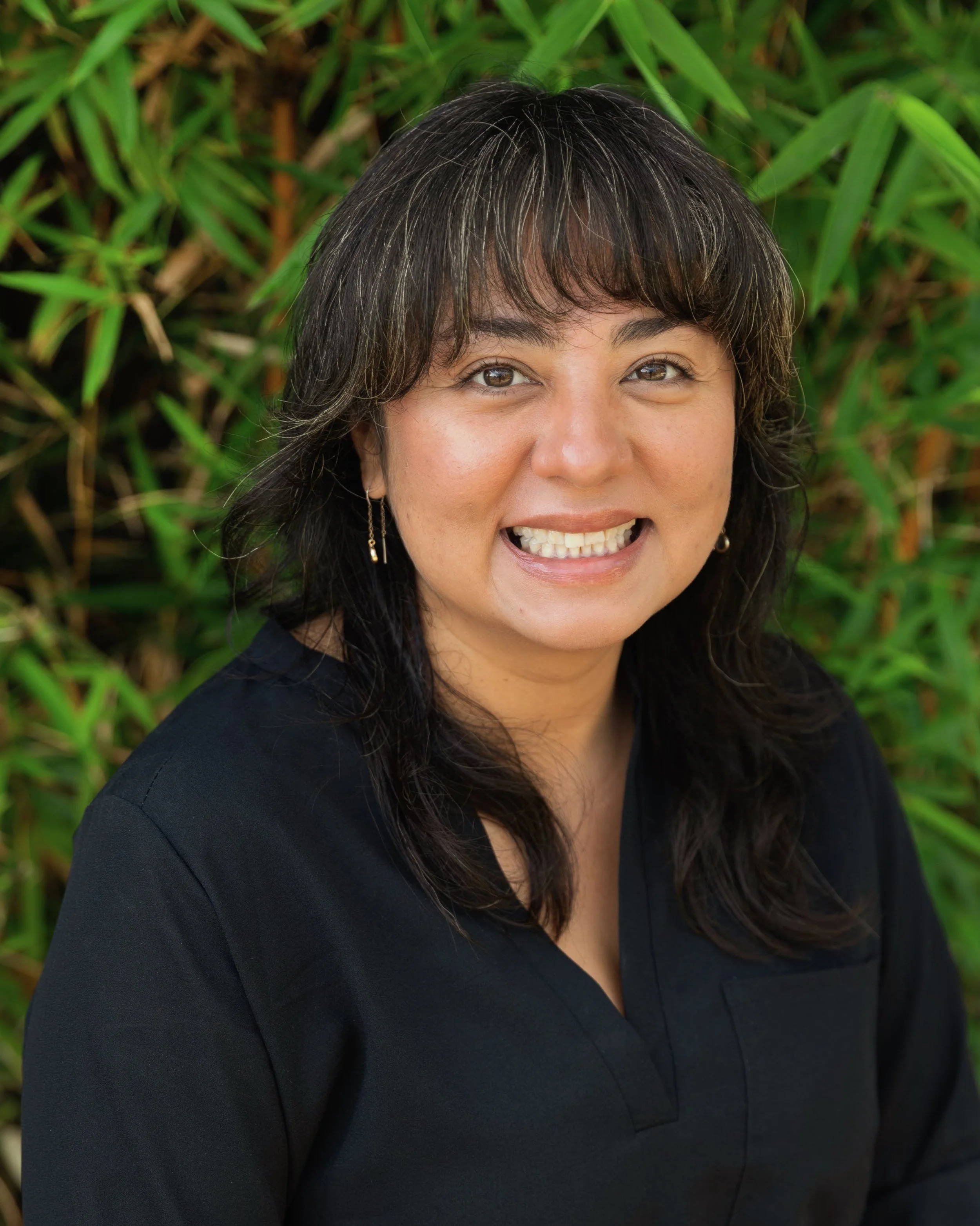 Zelzin Jiménez, Interim Director of Admissions, smiling in front of green foliage.