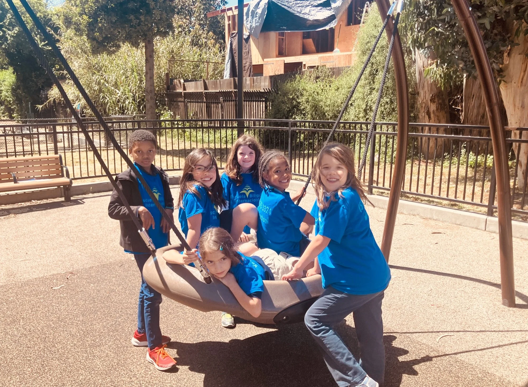 Young EBI students smiling together on a basket swing on the playground