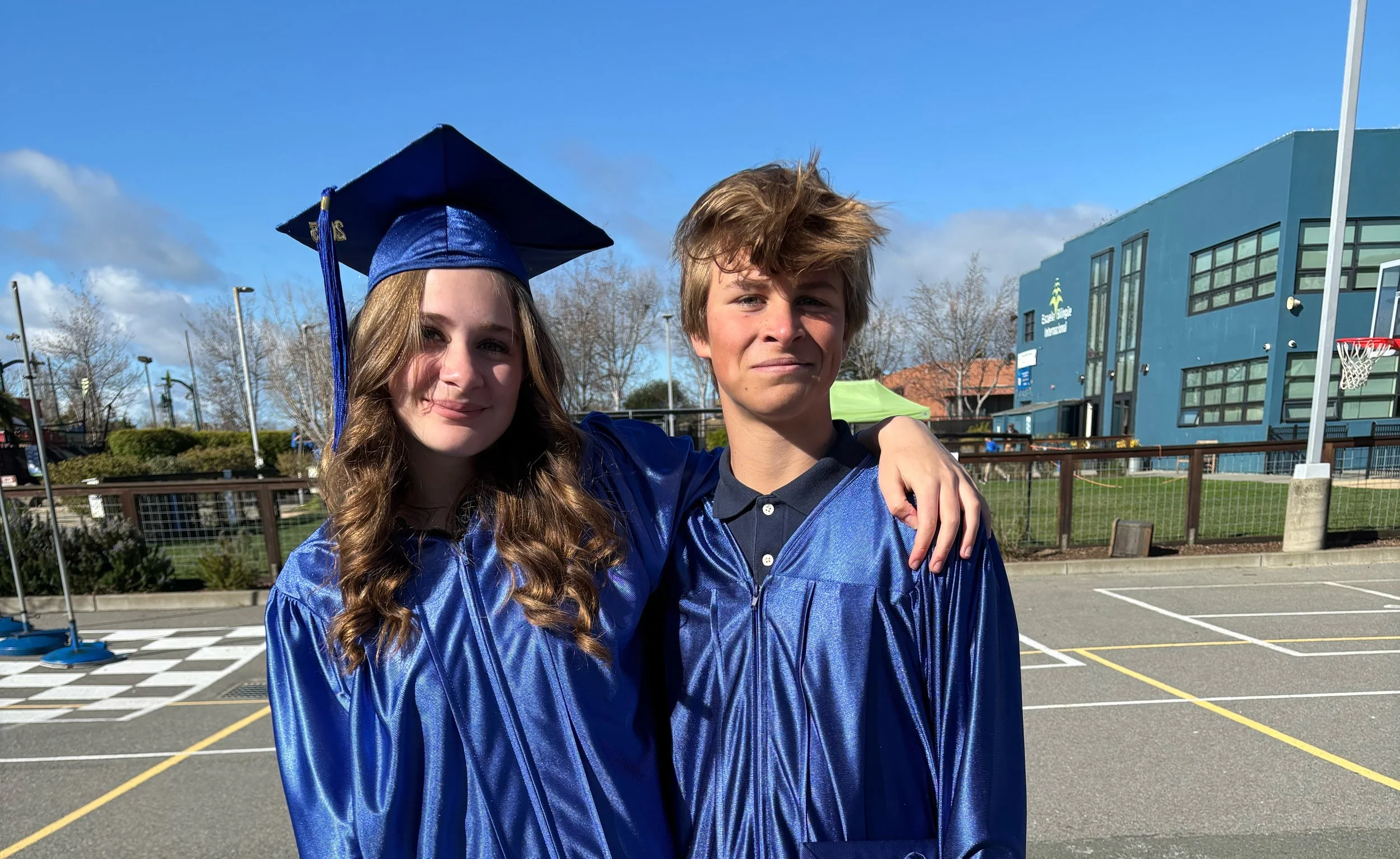 Two graduating students smile in graduation caps and robes