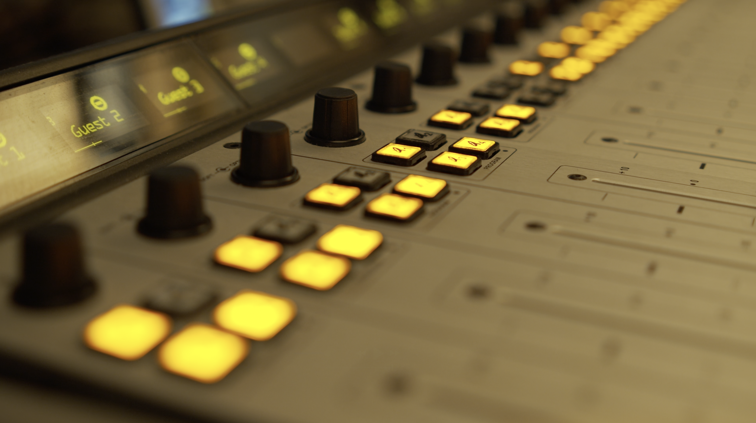 Close-up of a music mixing console with illuminated yellow buttons, knobs, and sliders.