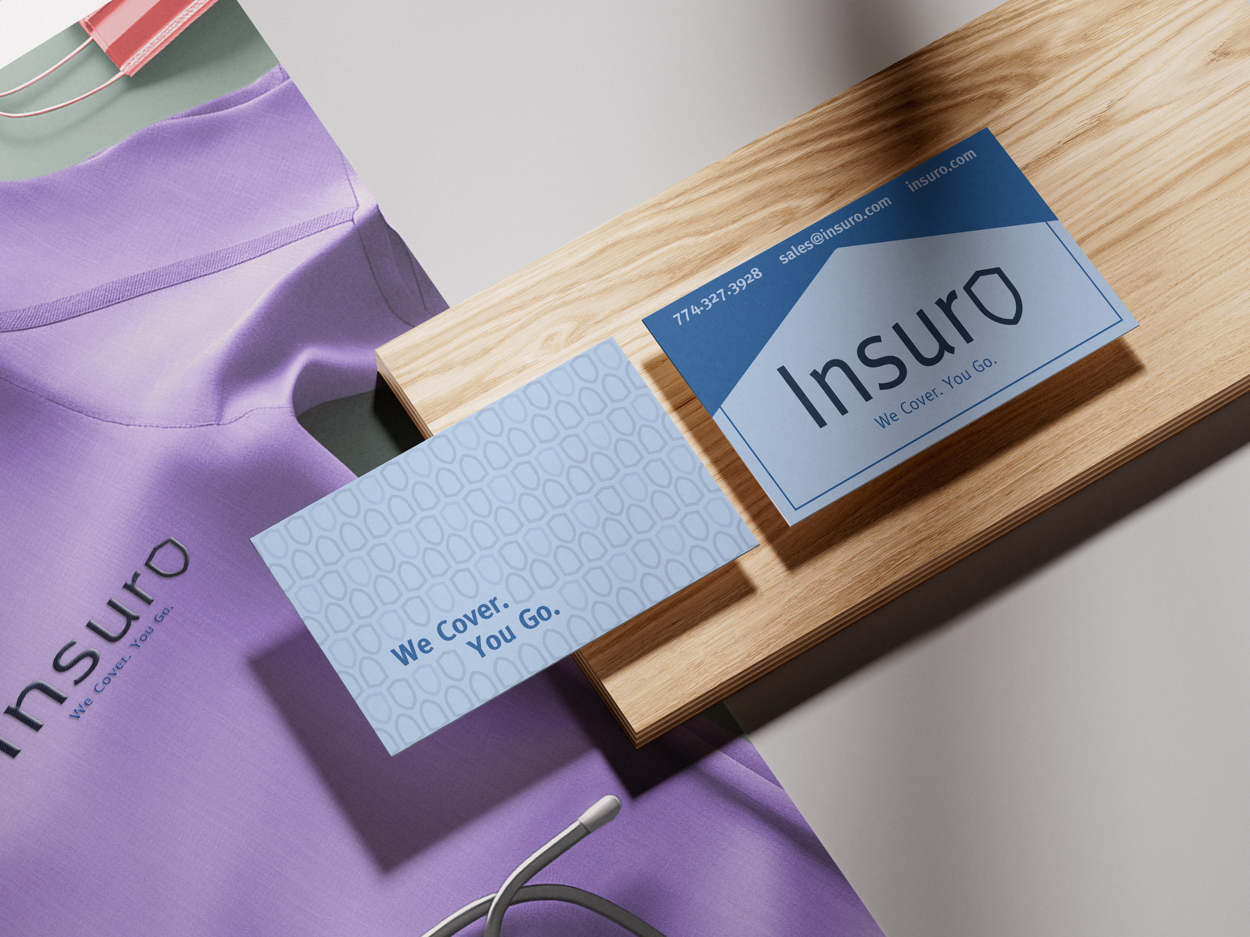 Business card placed on a wooden surface, partially covering a purple fabric item with the brand name 'Insuro' and the slogan 'We Cover. You Go.' Another card with the same branding and contact details is on top of the first card. made by vivfty!