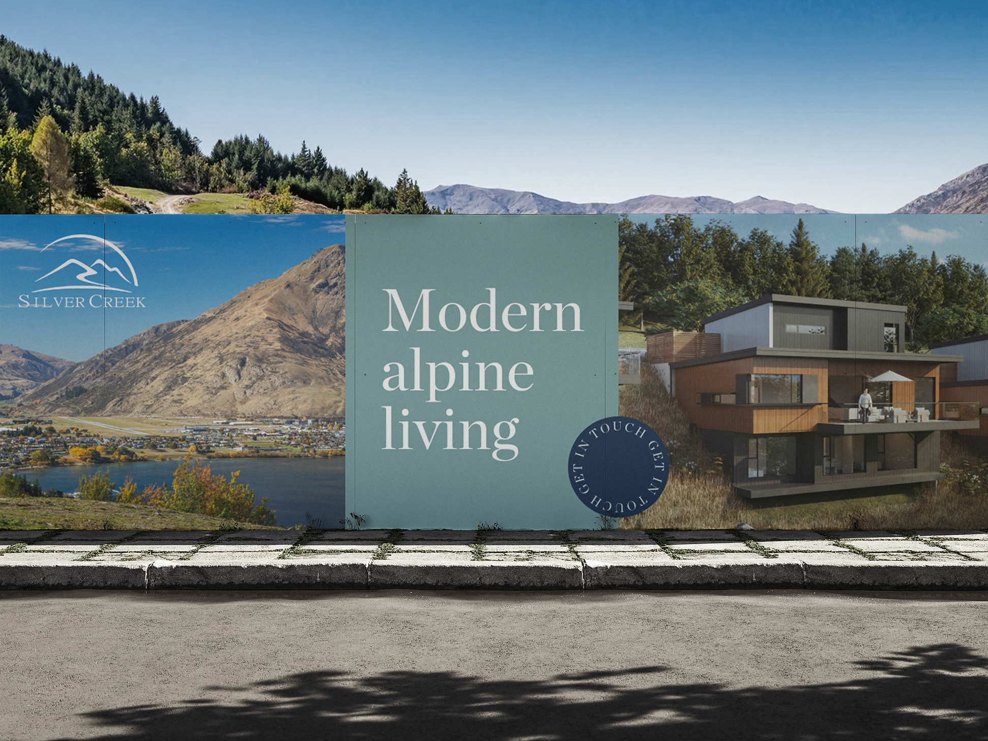 An outdoor billboard showcasing modern alpine living homes with scenic mountain and lake views in the background, featuring a contemporary house design and a logo for Silver Creek.