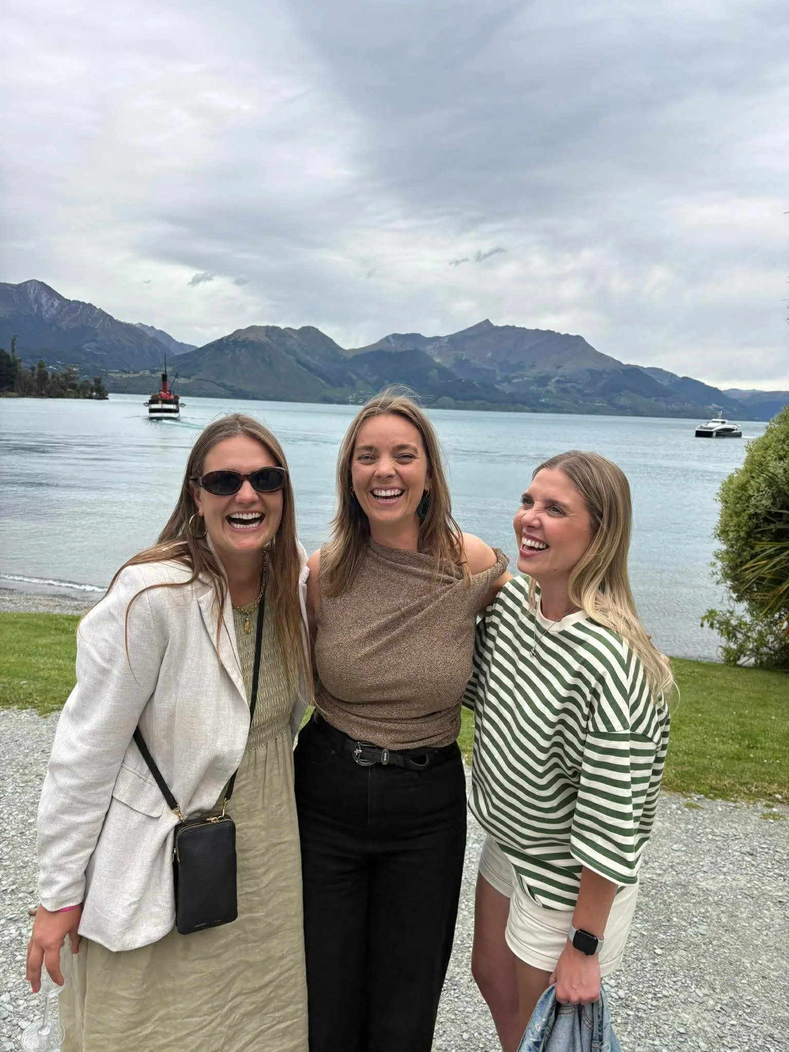 Unrule. Creative founders, smiling and laughing together outdoors near a lake, with mountains and boats in the background.