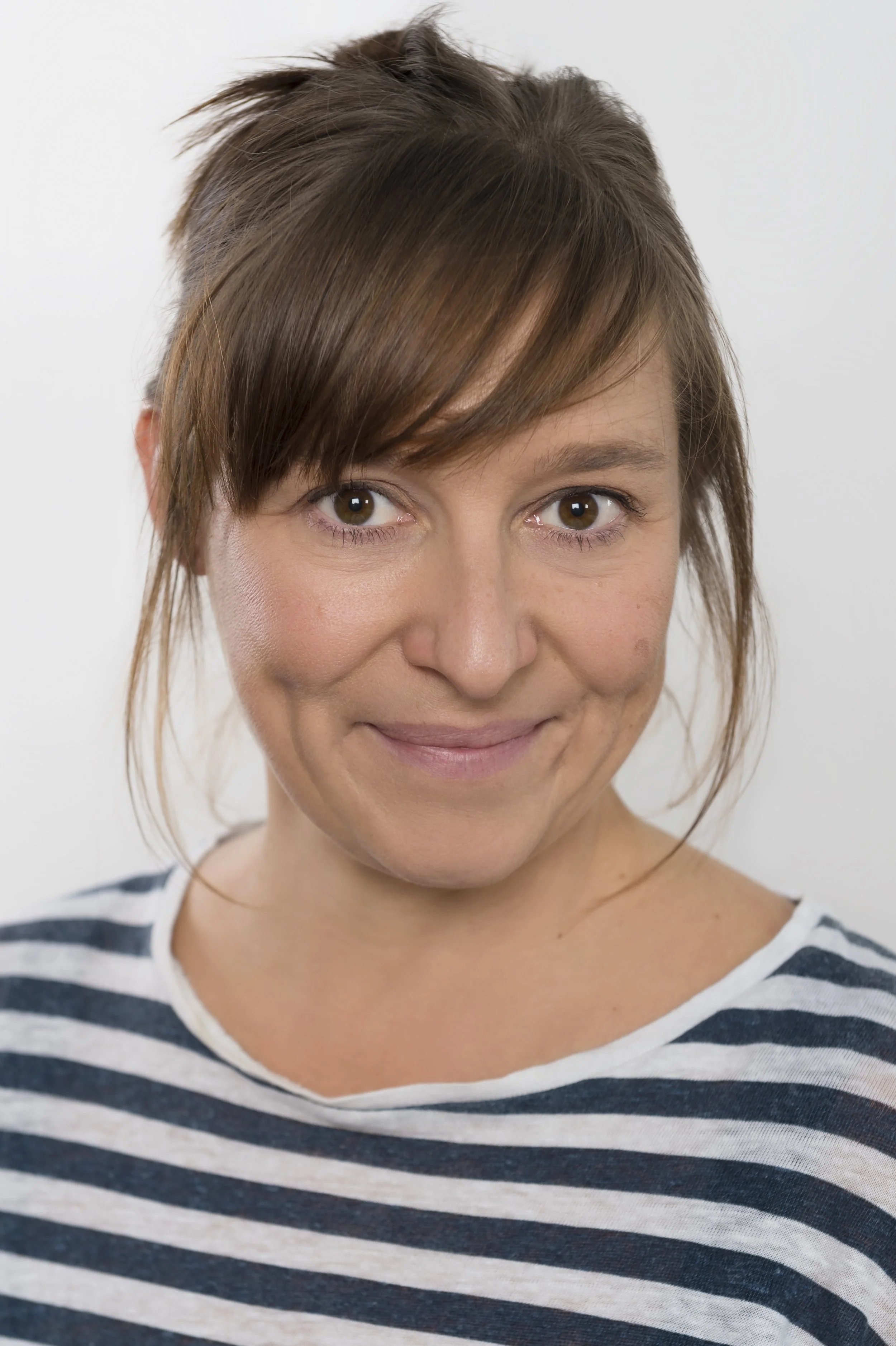 A woman with short brown hair, light skin, and brown eyes, wearing a white and navy striped shirt, smiling at the camera against a plain white background.