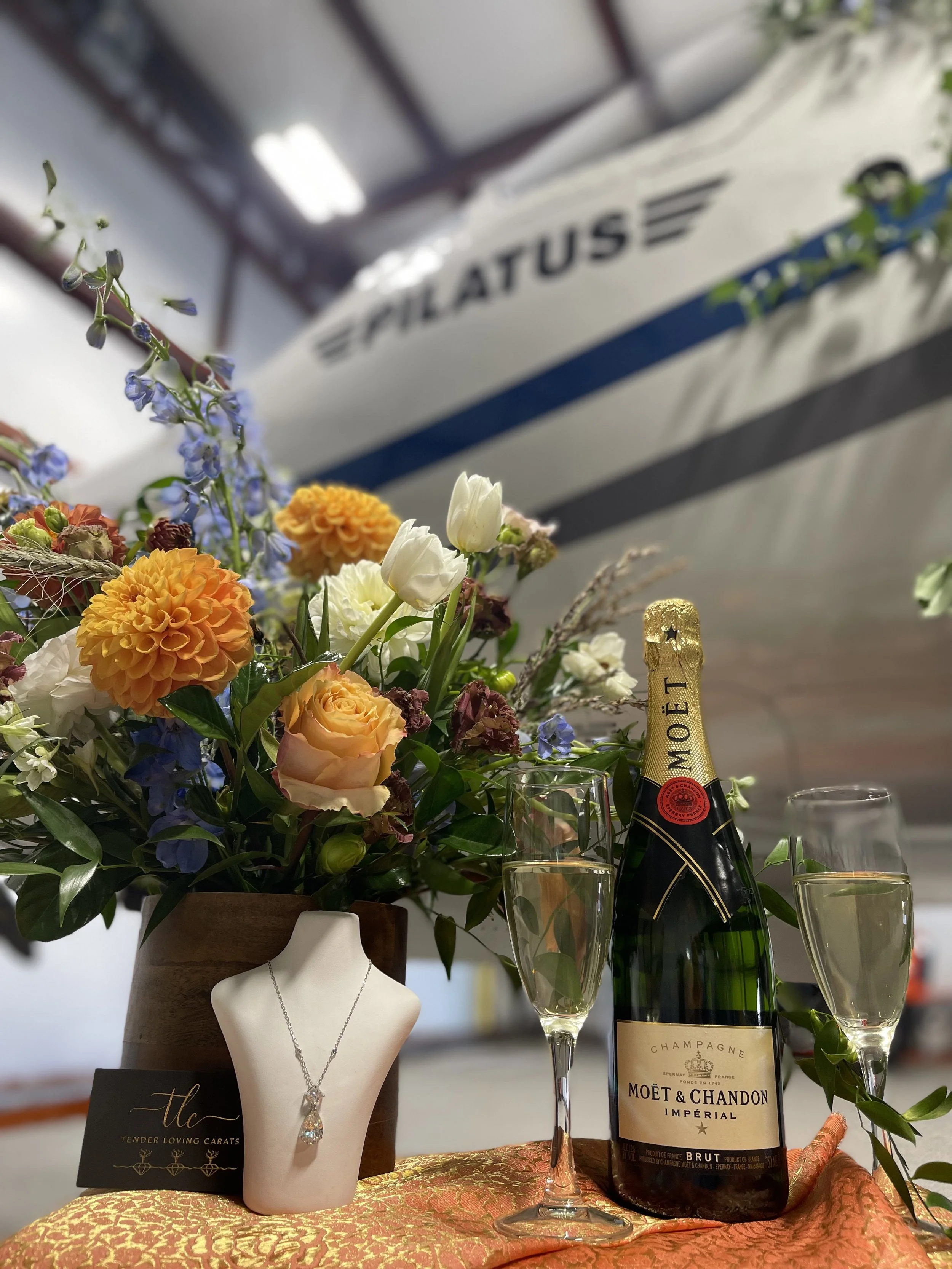 Luxury floral arrangement, Moët & Chandon champagne, and jewelry display beside a Pilatus aircraft — symbolizing an elegant private charter celebration.