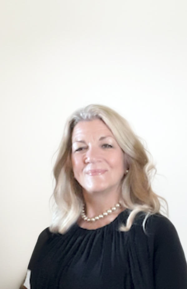 A woman with blonde hair wearing a black top and pearl necklace, smiling at the camera against a plain white background.