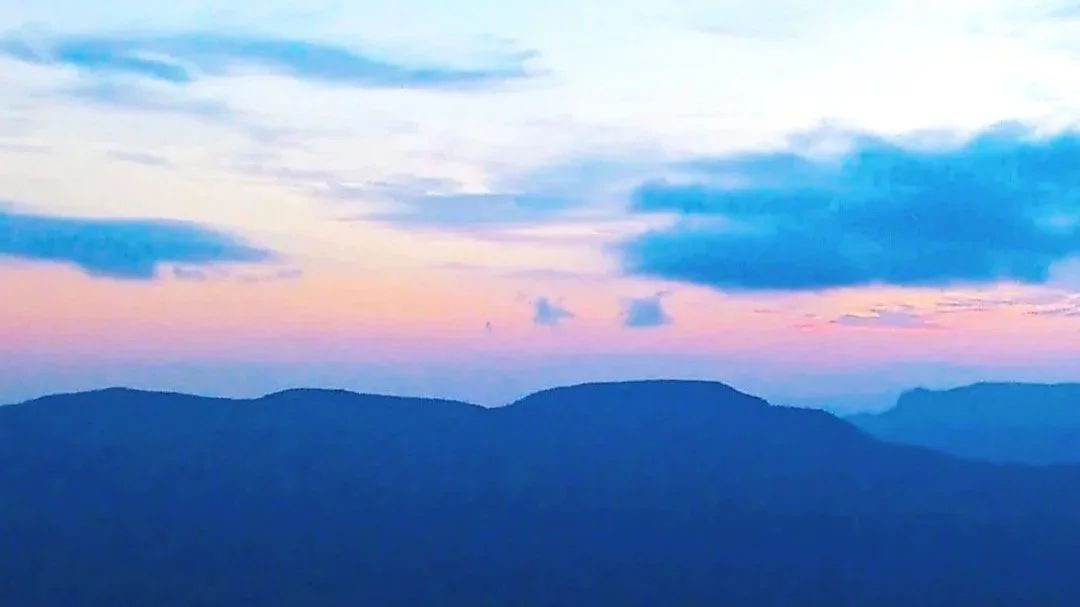 Sunset over mountain range with colorful sky including pink, blue, and purple hues, and scattered clouds.
