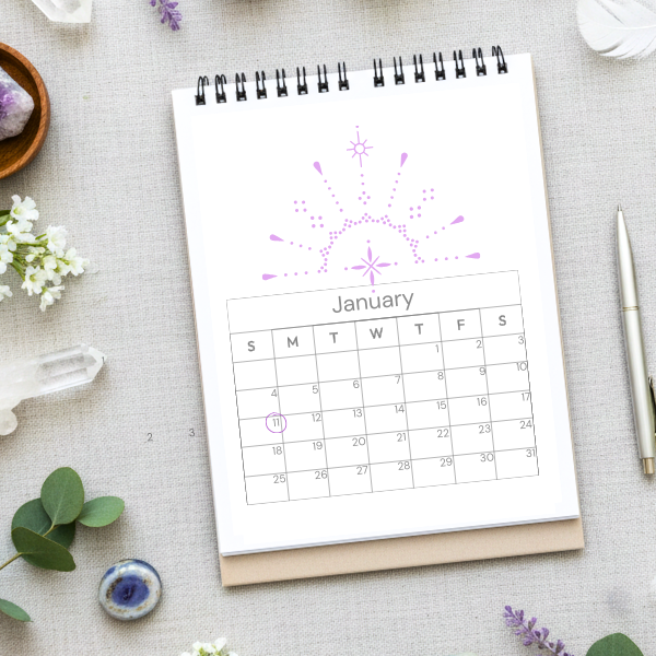 A top-down view of a white spiral notebook on a desk showing a January calendar with a purple sunburst design, surrounded by crystals and eucalyptus, marking the 111 Portal.