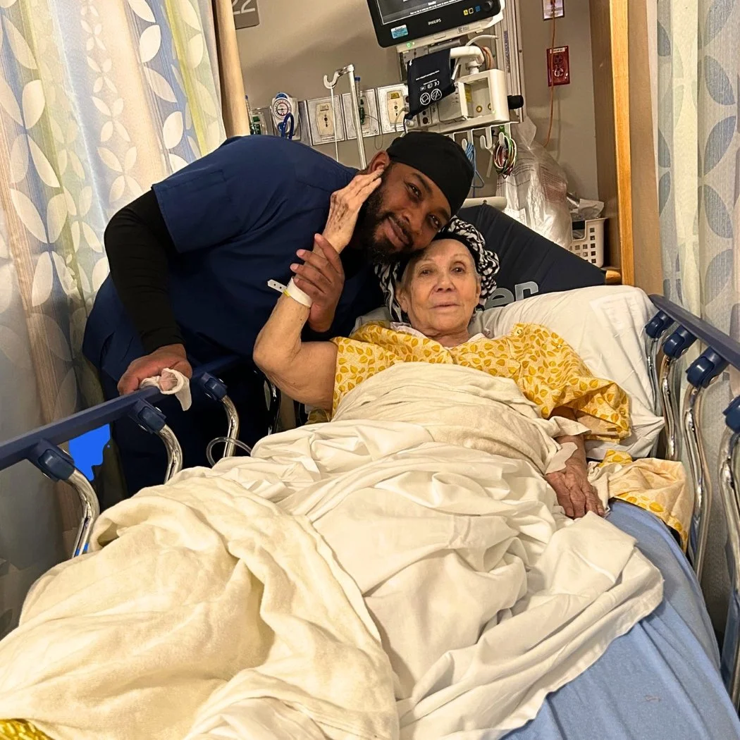 A healthcare worker smiling beside an elderly woman resting in a hospital bed, embodying The Nenita Foundation’s commitment to elderly care, compassion, and dignity.