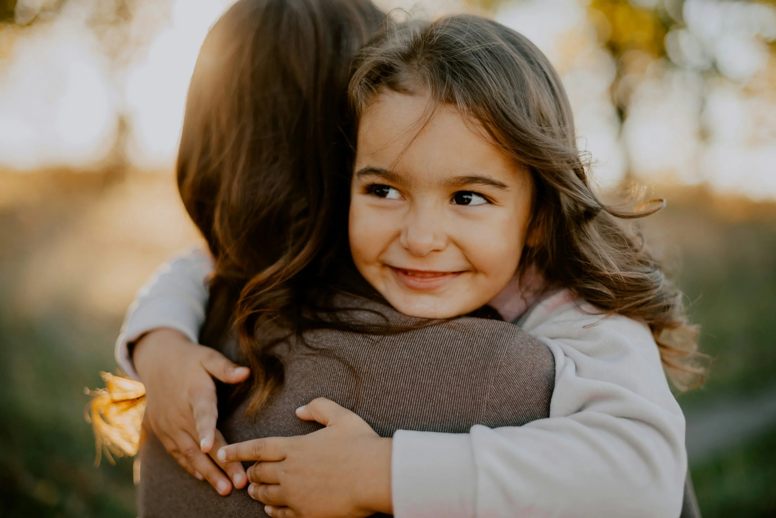 A young girl hugging an adult outdoors with sunlight filtering through trees, reflecting The Nenita Foundation’s mission to create safe and nurturing environments filled with love, trust, support, and security.