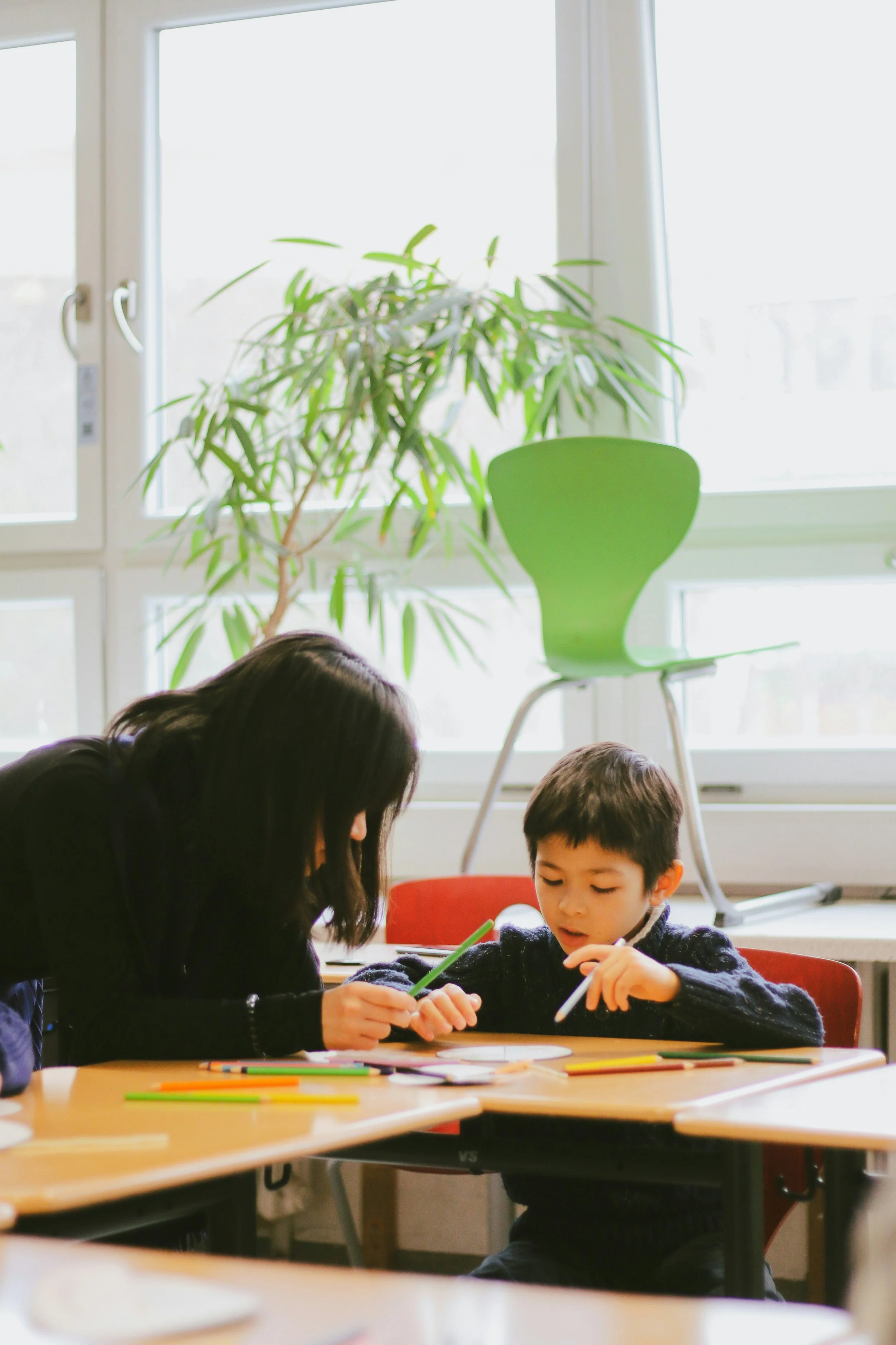 A teacher and young boy sitting together at a table, engaging in a colorful learning activity with markers, representing The Nenita Foundation’s child academic and confidence-building programs.