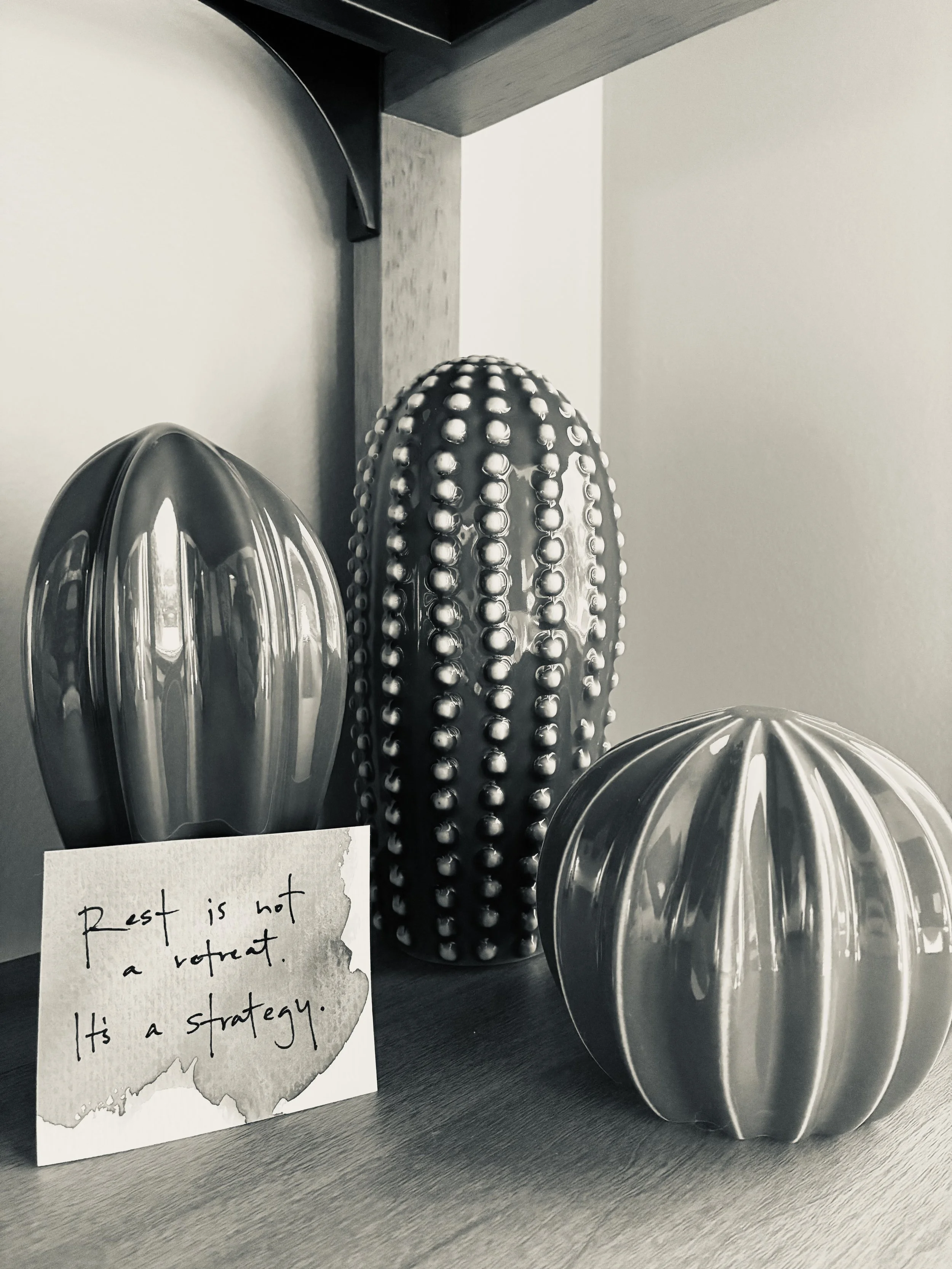 Metallic decorative objects with dotted and striped patterns, and a handwritten note that says 'Rest is not a reward. It’s a strategy'.