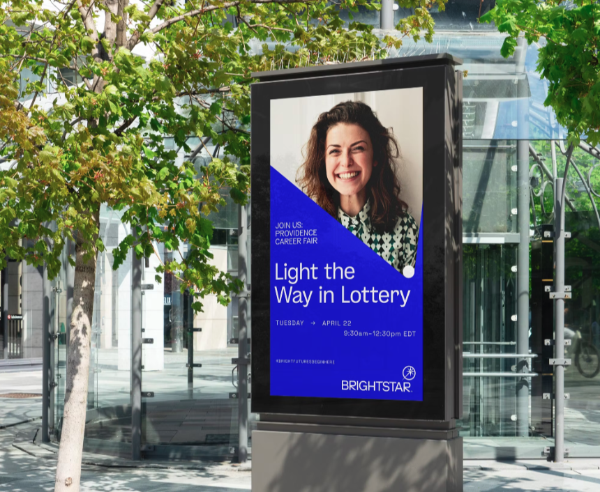 Digital advertisement at a bus stop promoting a career fair with the message 'Light the Way in Lottery'. The ad features a smiling woman with curly hair and a patterned shirt, and includes details about the event date, time, and location.