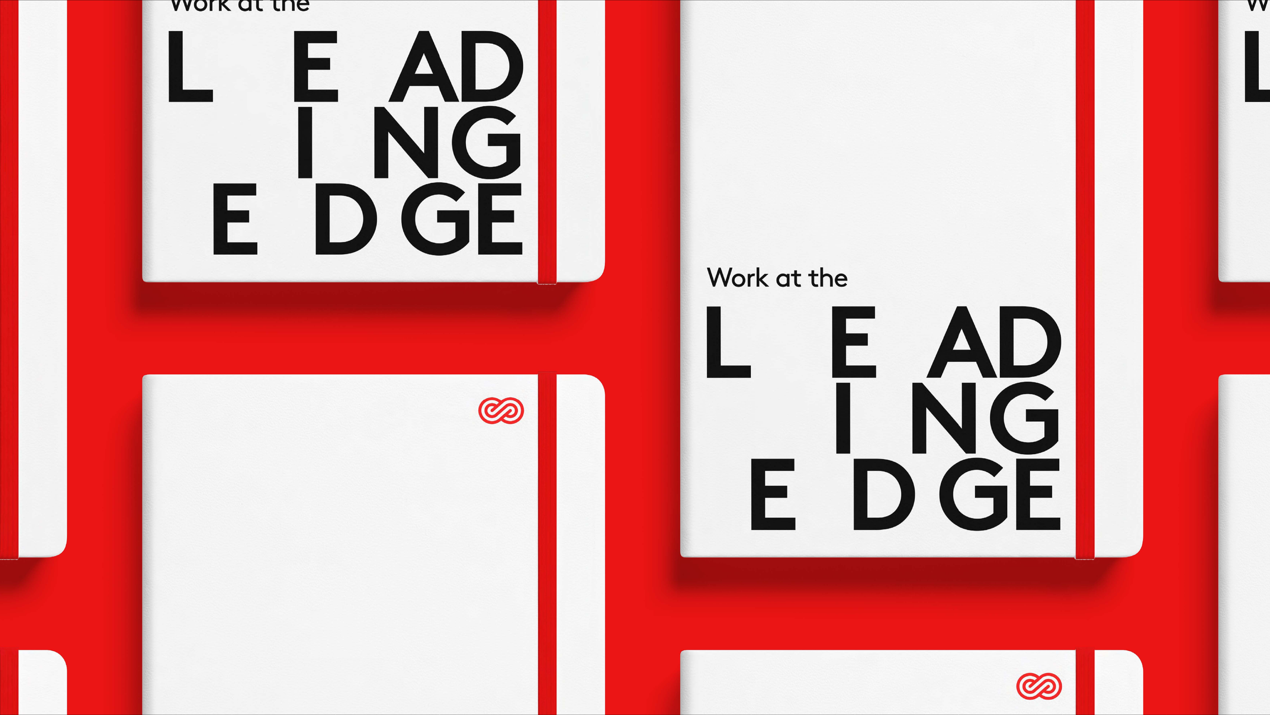 Multiple white notebooks with black text that reads 'Work at the LEADING EDGE,' placed on a red background. Red elastic bands hold the notebooks closed.