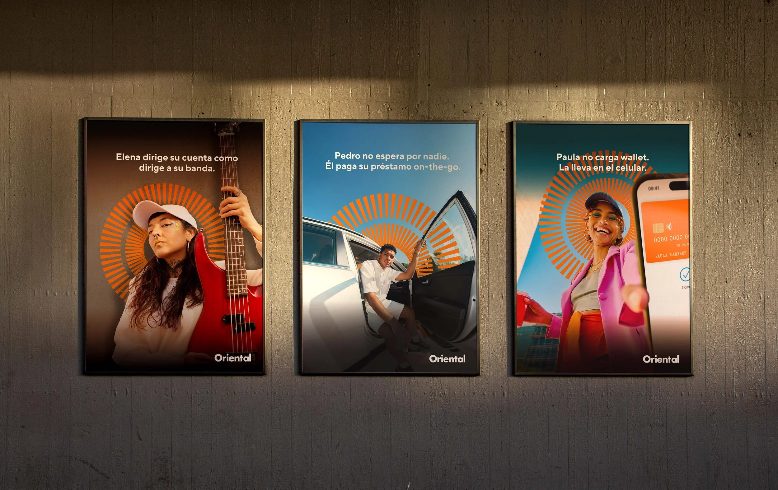 Three posters on a wall, each featuring a person with a circular orange pattern behind them and Spanish text. The first shows a woman with long dark hair, wearing a white cap and jacket, holding a red guitar. The second features a man sitting by an open car door, wearing a white shirt, with the door open and a bright blue sky. The third displays a smiling woman with a cap, holding a smartphone, with a sunset or sunrise background.