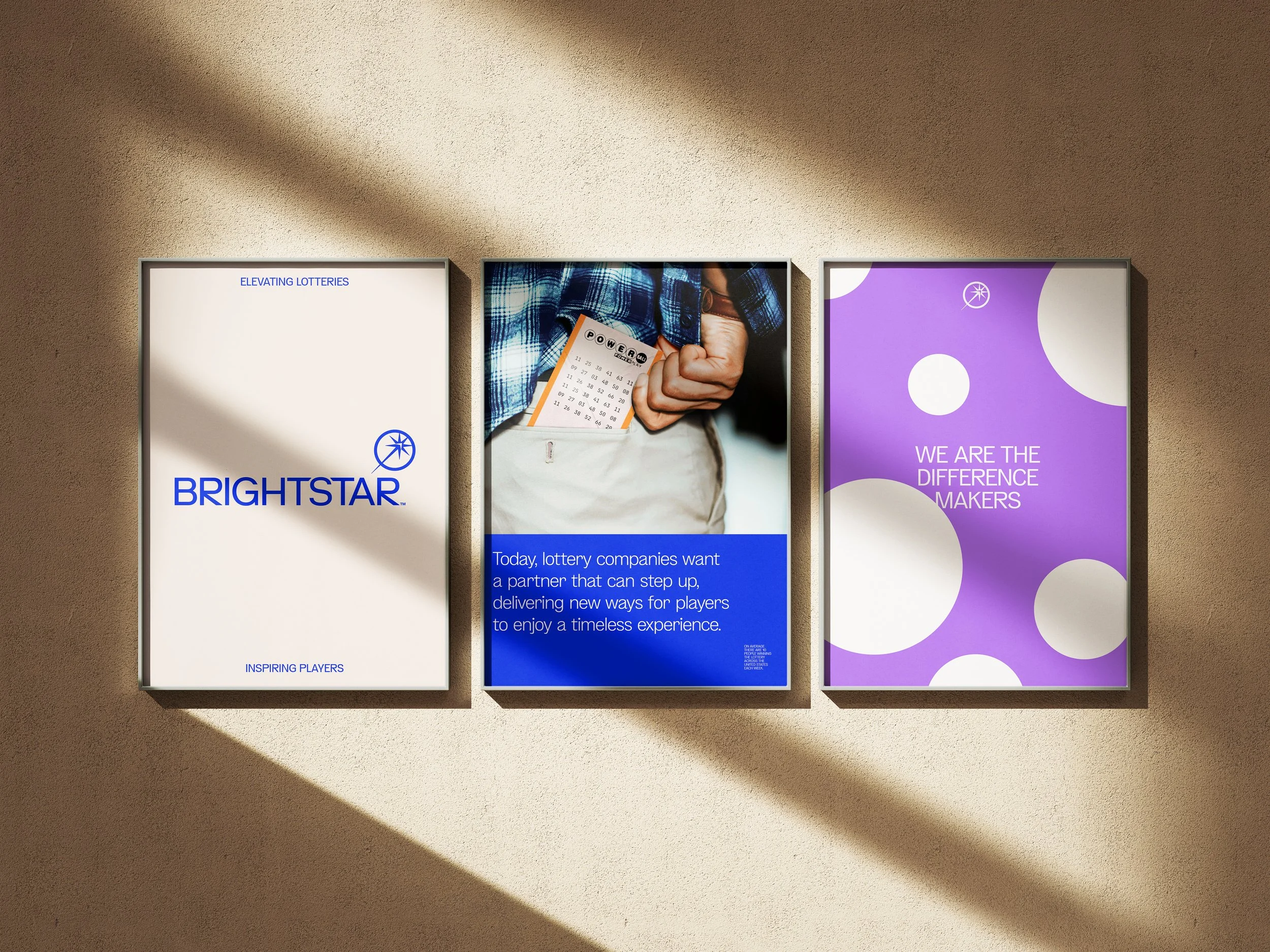 Three illuminated advertisements on a beige wall, with shadows cast diagonally across them. The first displays the BrightStar lottery logo with the tagline "Inspiring Players." The second features a person in a plaid shirt holding a lottery ticket, with a blue text box explaining the company's goals. The third shows a purple background with white circles and the text "We are the difference makers."