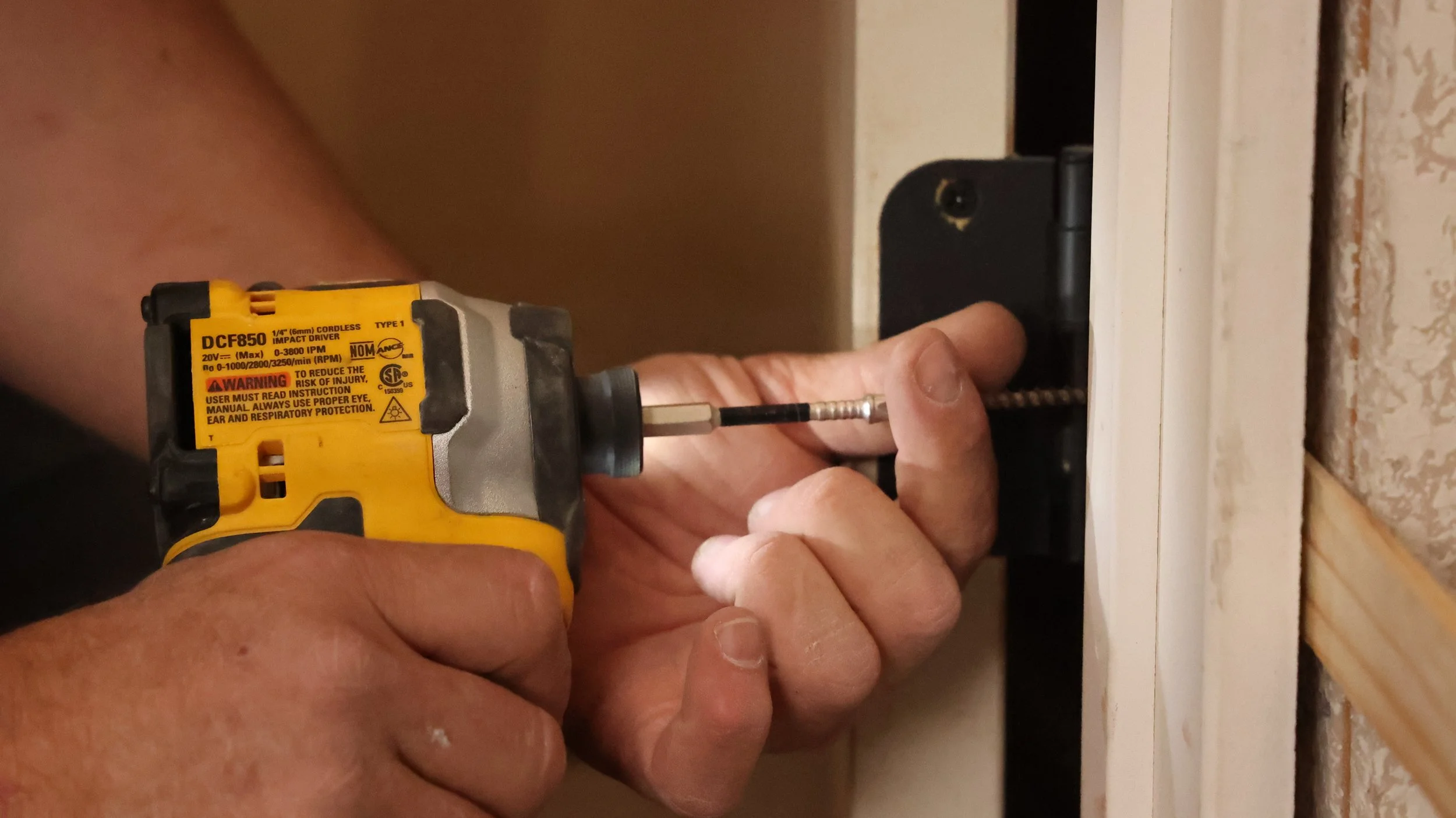 A person using a yellow cordless impact driver to work on electrical wiring inside an electrical box on a wall.