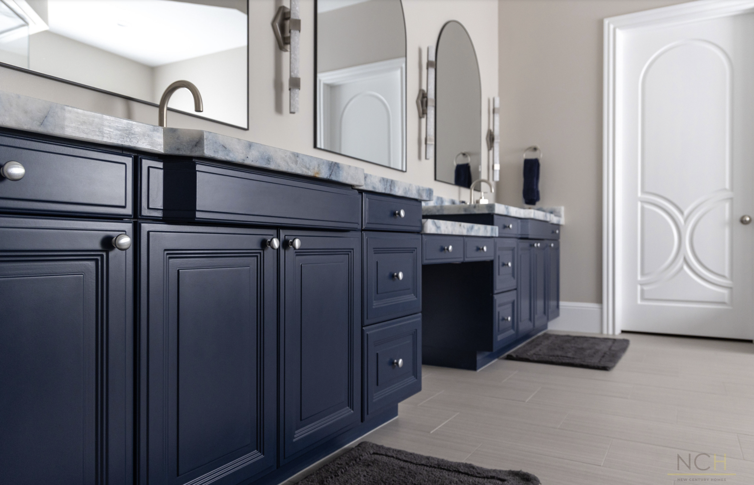 Modern kitchen with dark blue cabinetry, marble countertop, rectangular mirror, and white door with an arched panel design.