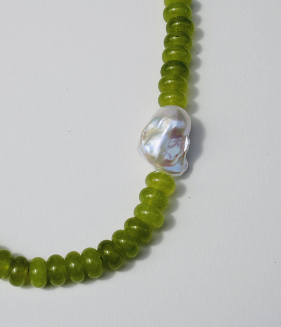 handmade Green jade beaded necklace with a large, irregularly shaped white baroque pearl pendant on a white background.