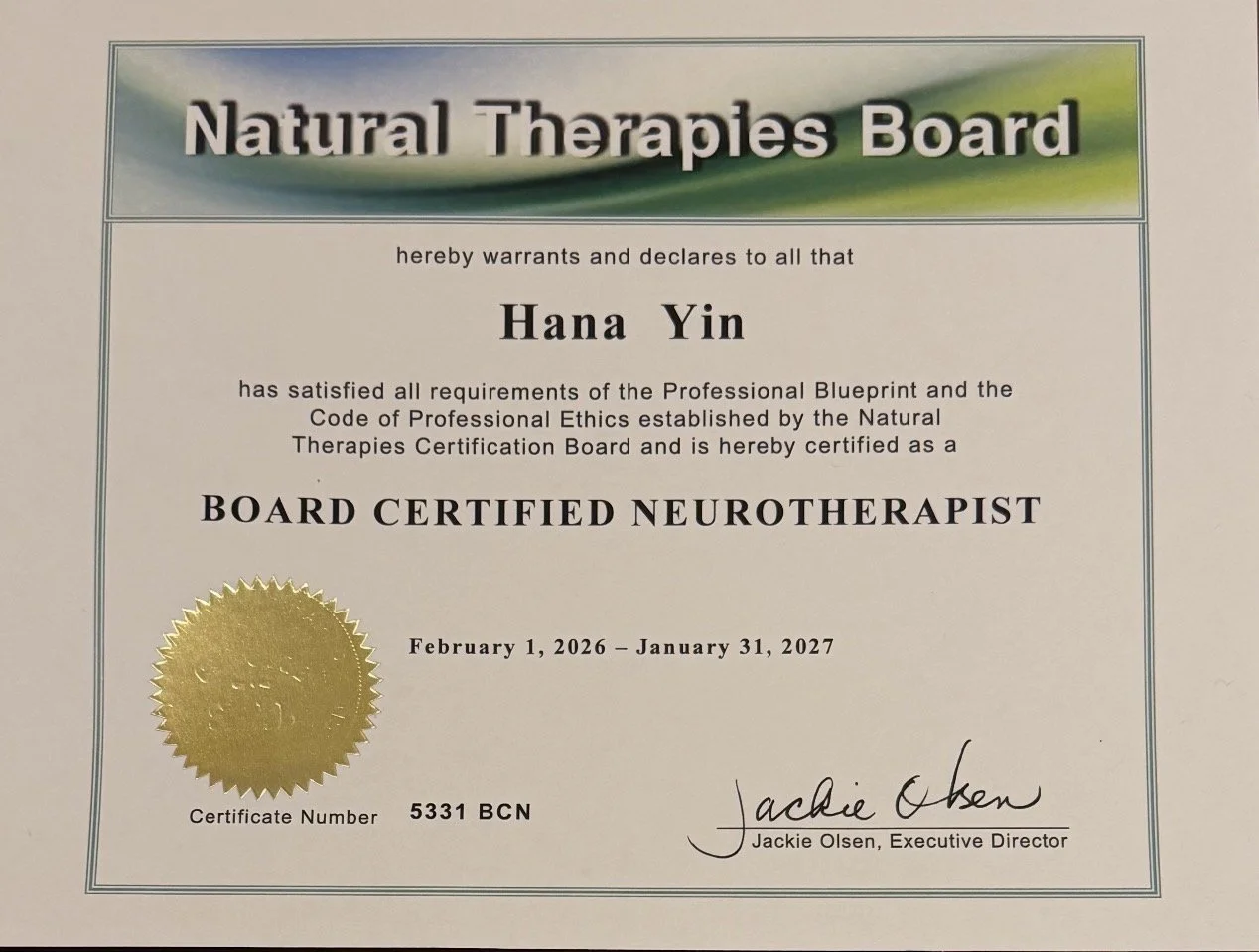 Hana Yin (PhD, LMFT, BCN), a board certified neurotherapist, with a gold seal and signature from Jackie Olsen, issued between February 1, 2026, and January 31, 2027.