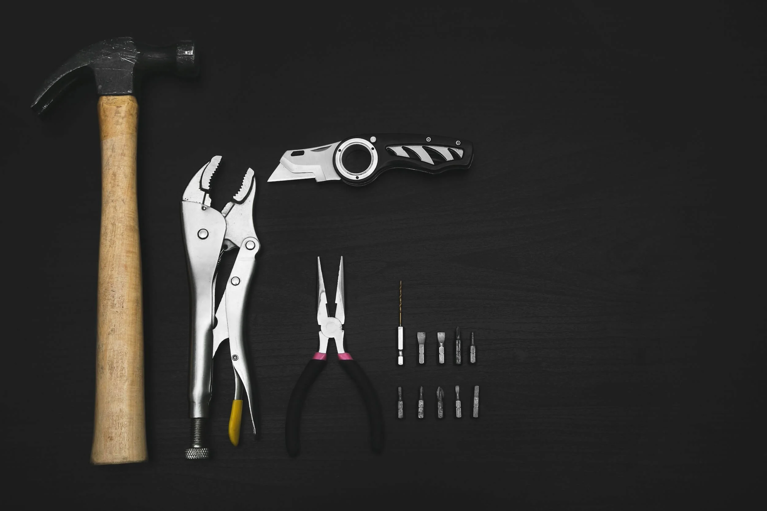 flatlay image of hammer, pliers and other tools on black surface