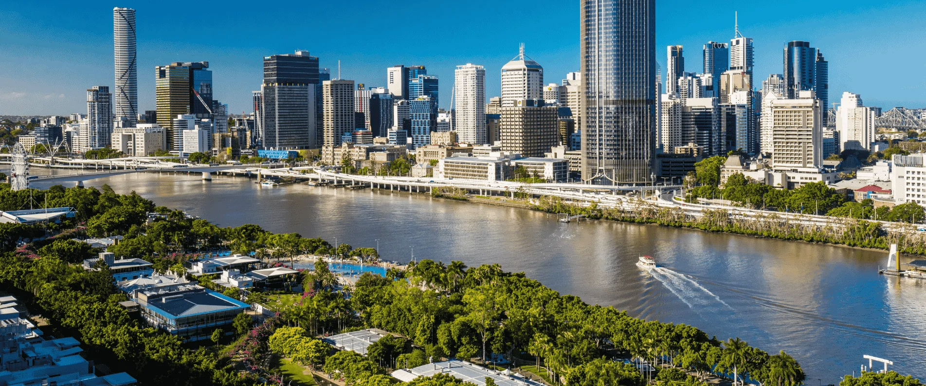 City skyline of Brisbane, Australia, with tall modern buildings, a river with a boat, and green parks along the waterfront.