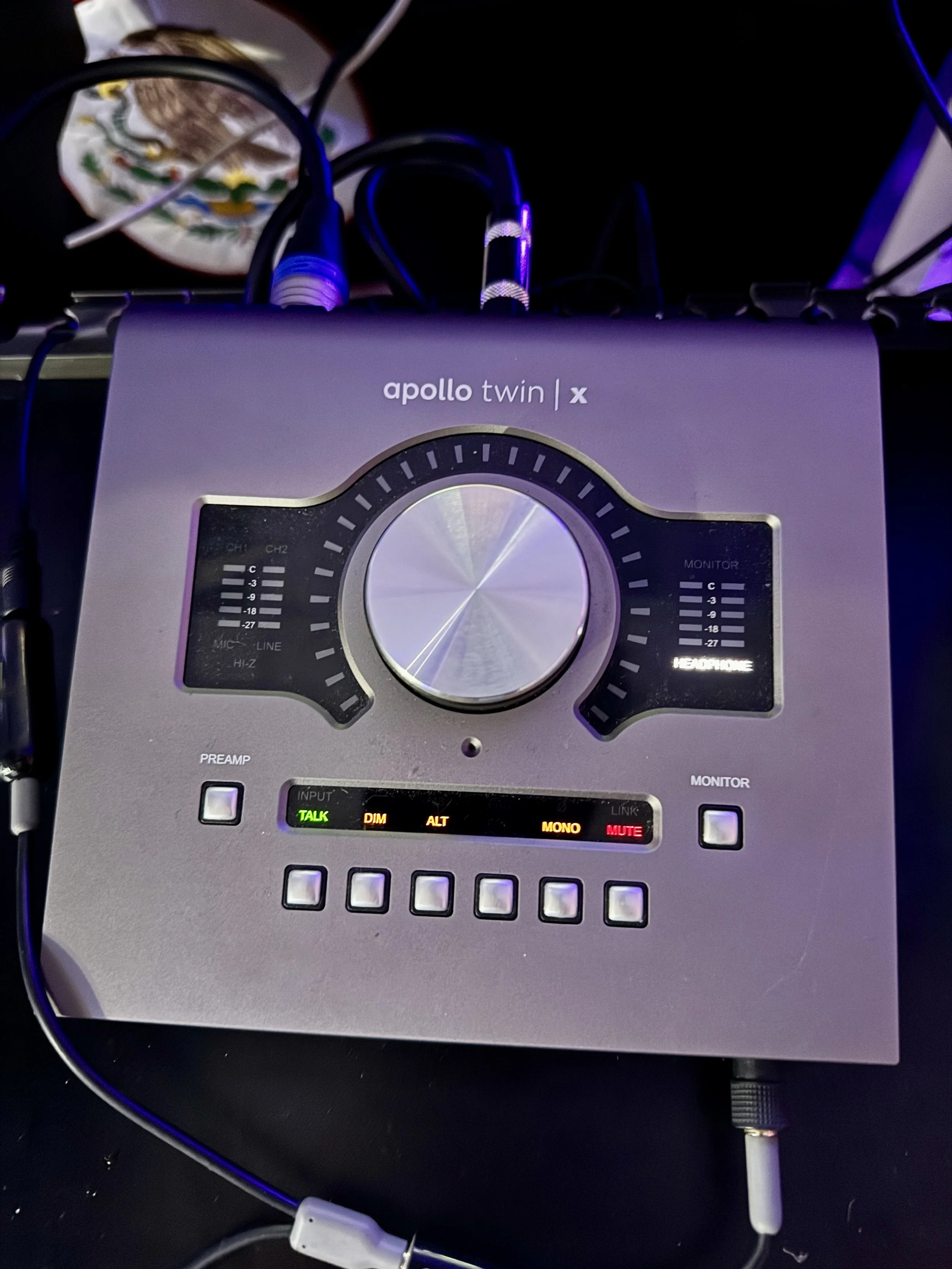 A silver audio mixer with the label 'apolo twin x', featuring multiple dials, buttons, and LED meters, connected to several cables.