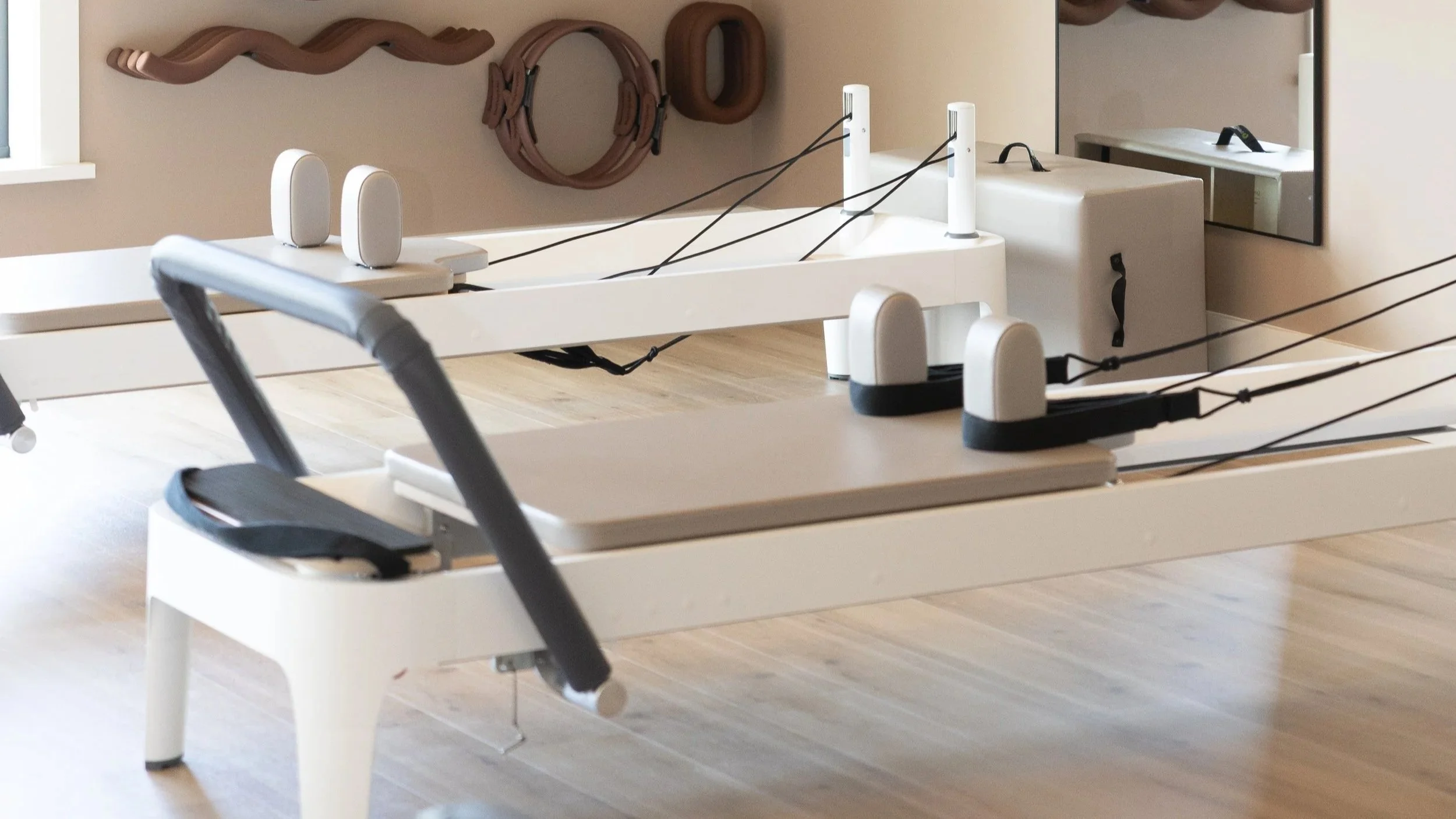 Rowing machines in a fitness room with a mirror and wooden flooring.
