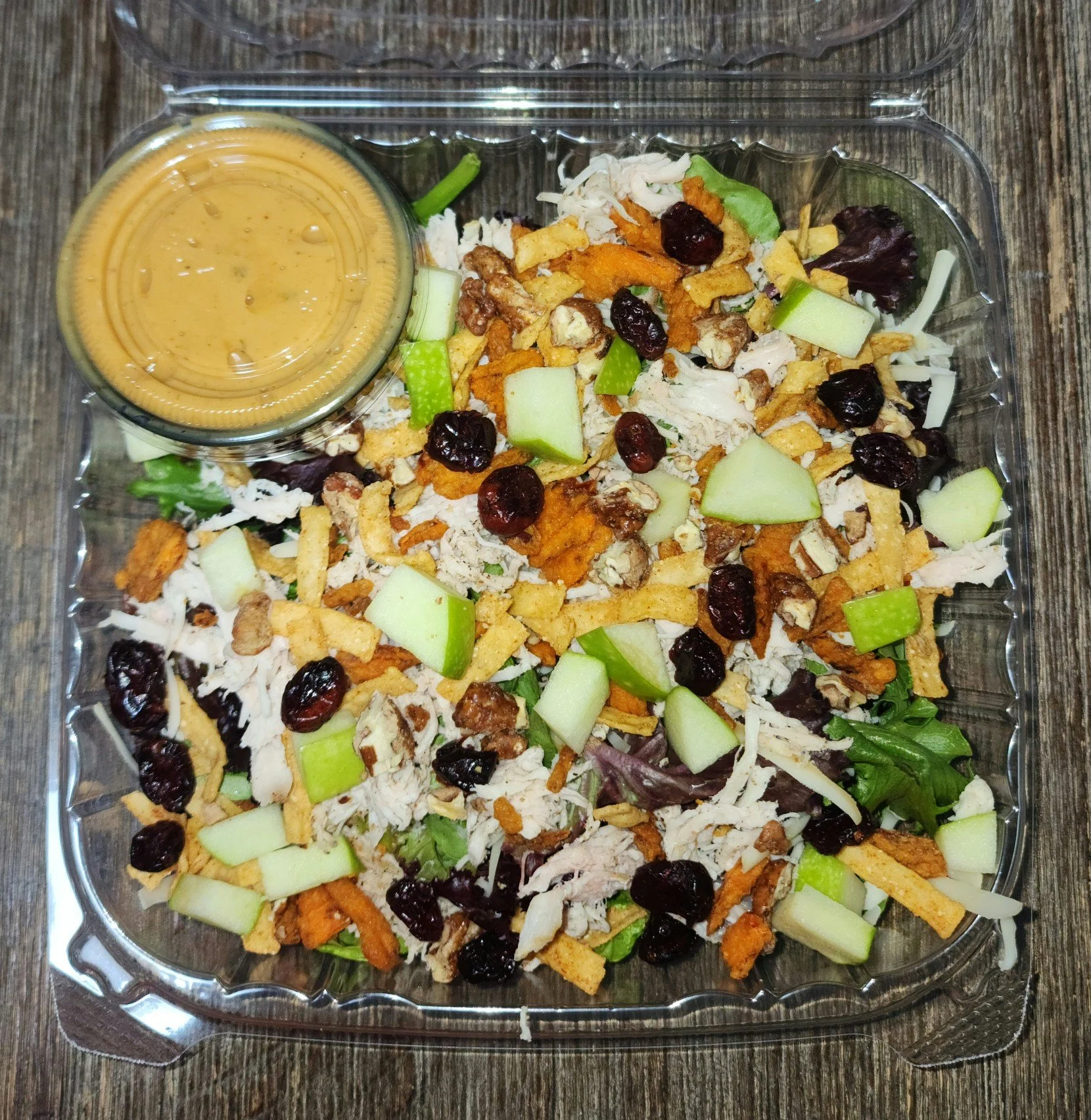 Container of chicken salad with chopped chicken, green apples, dried cranberries, walnuts, crispy noodles, and a side of honey mustard dressing. Only served at Baked!