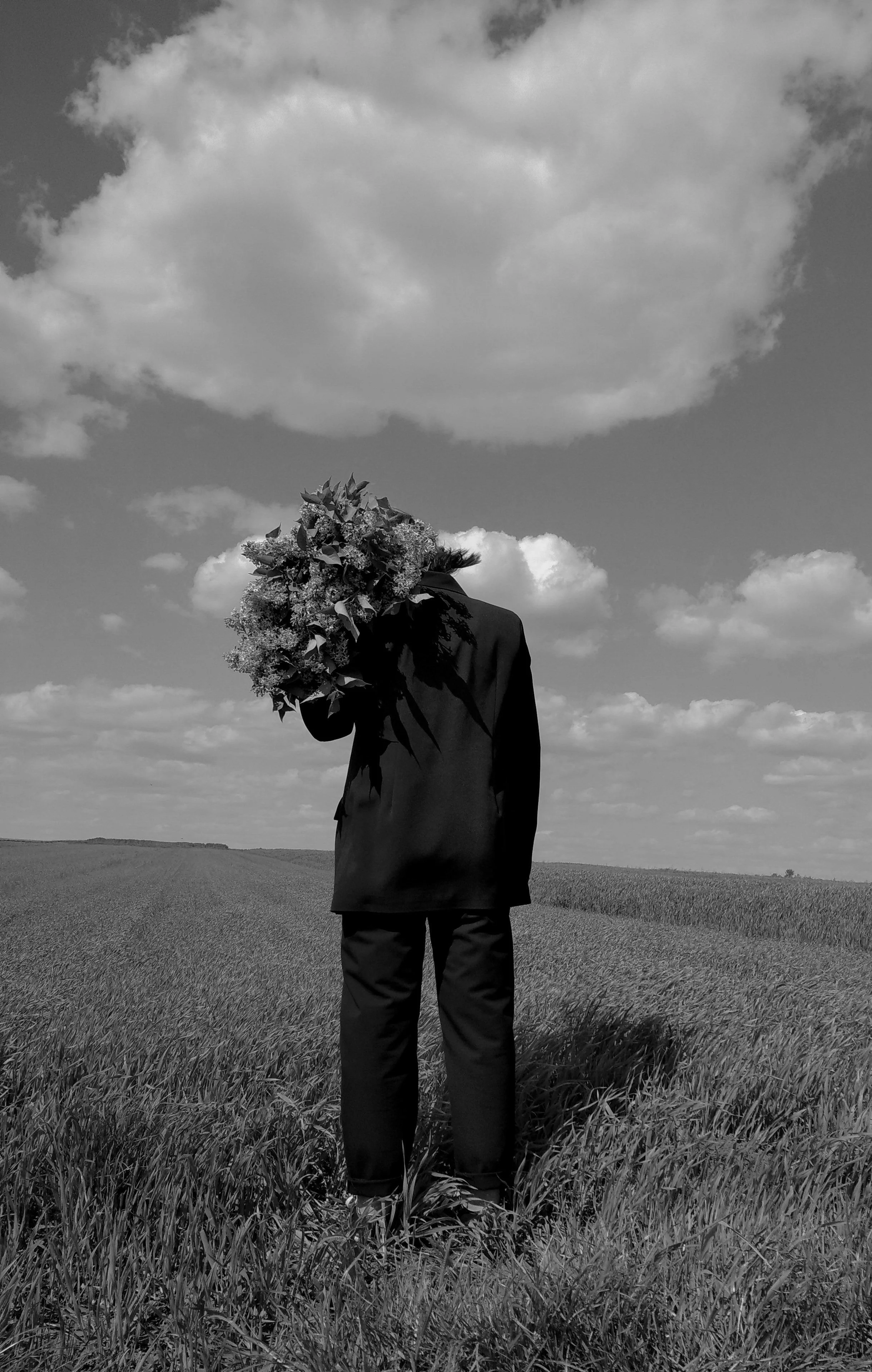 Black-and-white photo of a person in a field holding a large bouquet of flowers, with dramatic clouds overhead