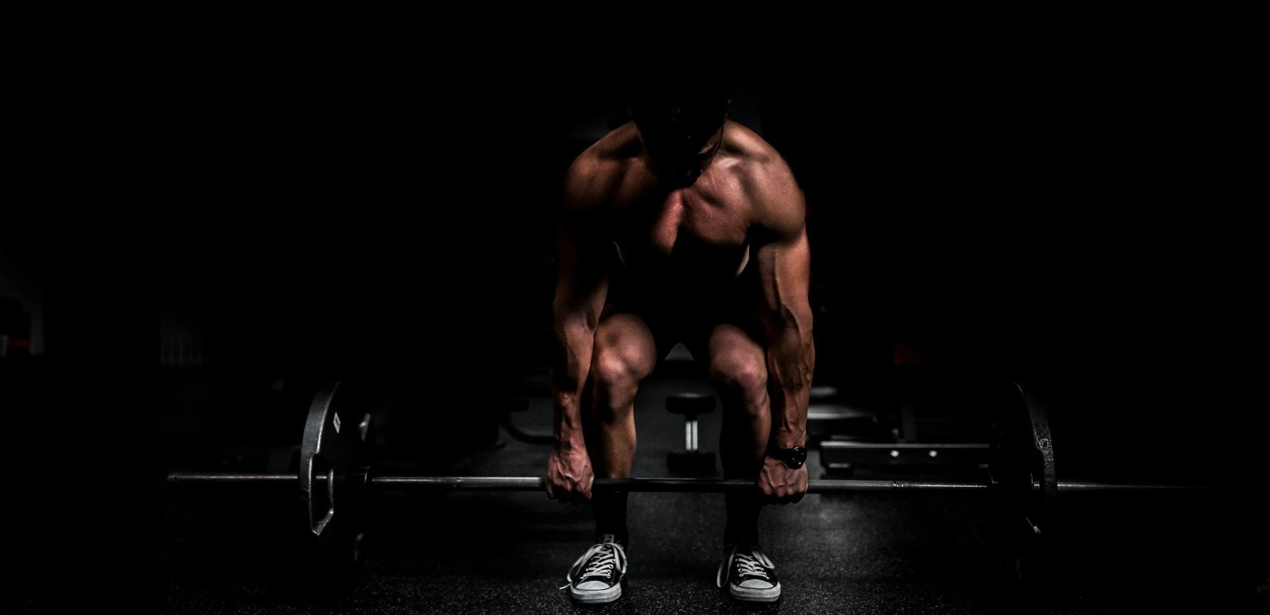 Mature lifter using blood flow restriction bands during deadlift workout in dramatic dark lighting