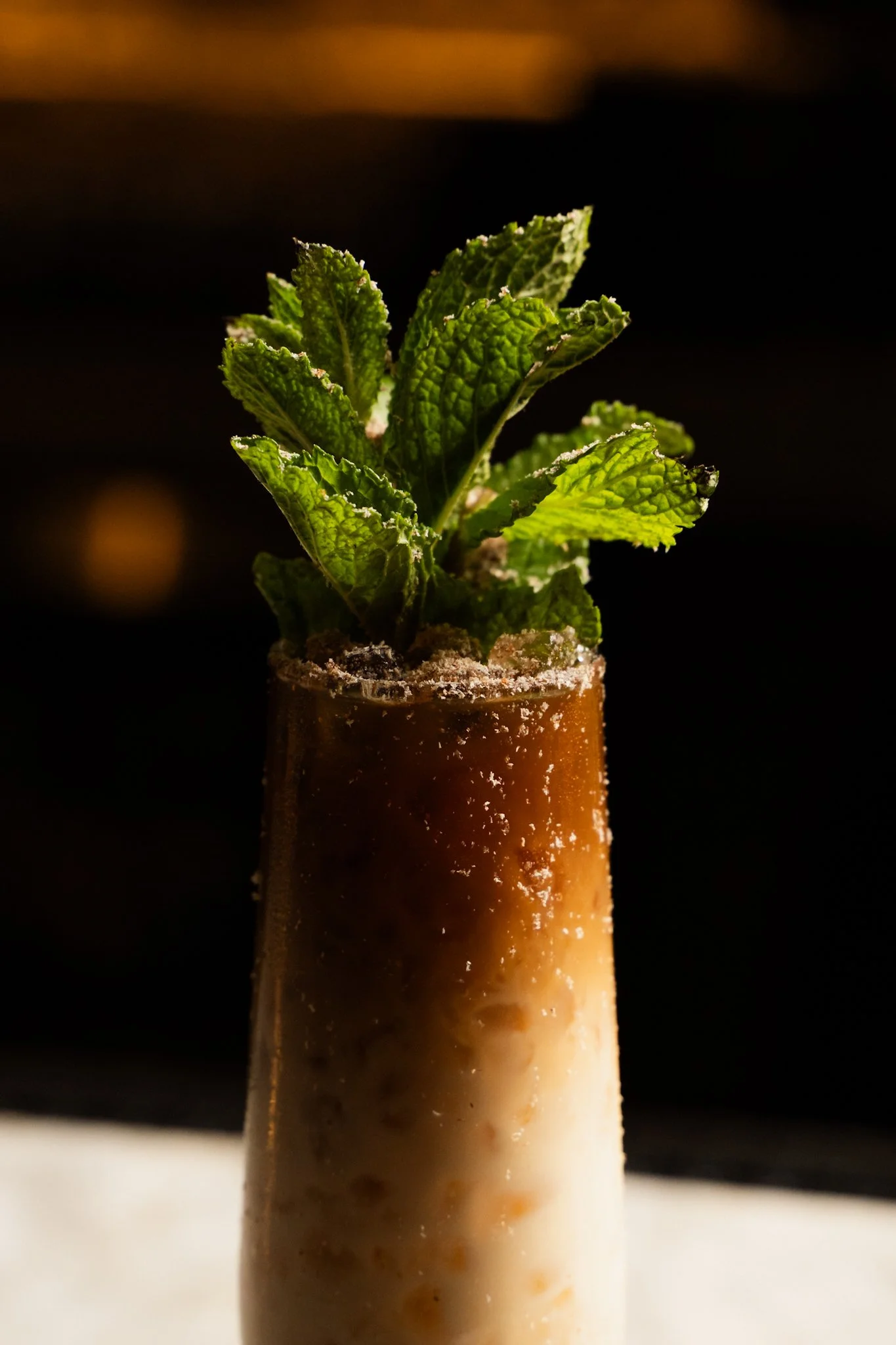 A layered iced coffee cocktail garnished with fresh mint leaves in a tall glass with condensation on the outside.