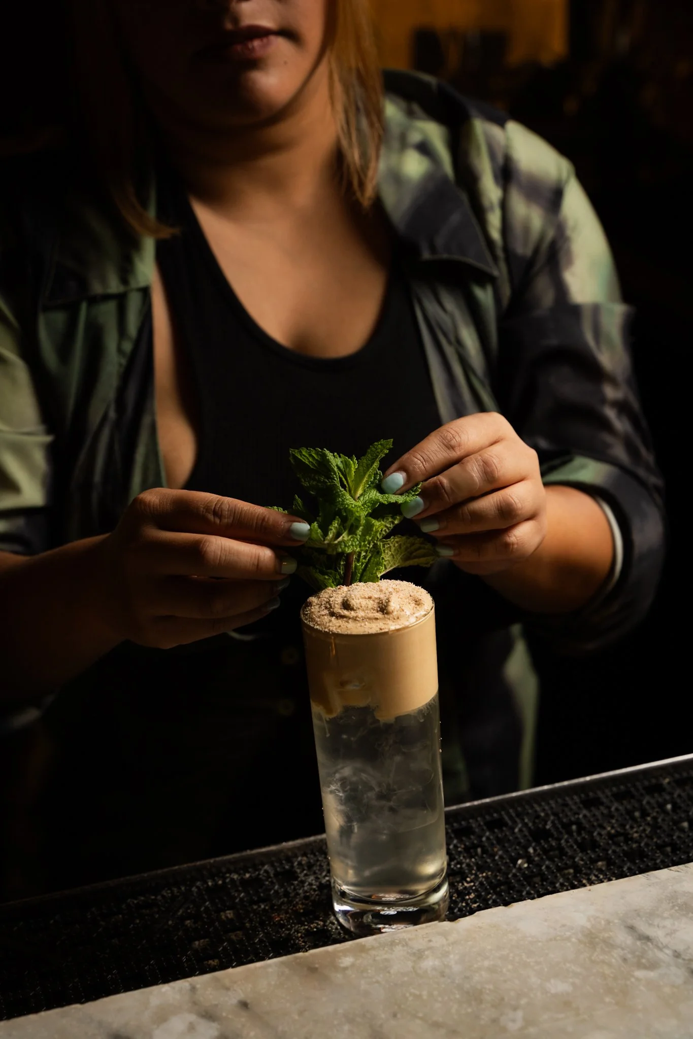 A woman is preparing a cocktail garnished with fresh mint leaves at a bar.