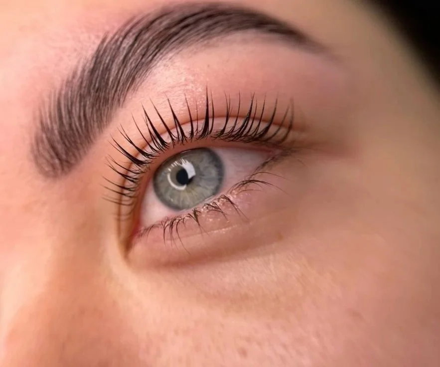 Close-up of a person's eye, showing blue iris, long eyelashes, and groomed eyebrow.