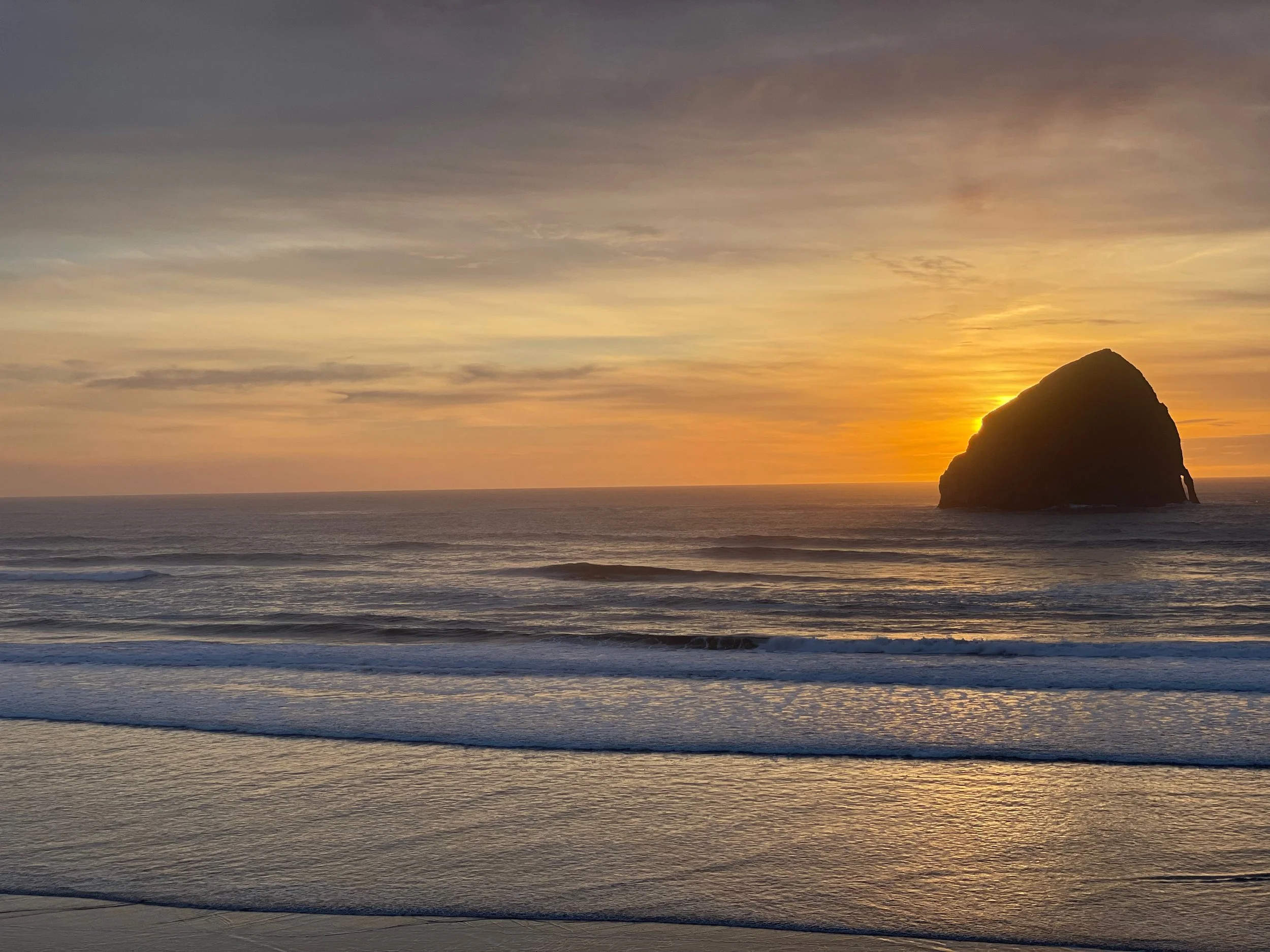 Sunset over the ocean with a large rock formation in the water on the right