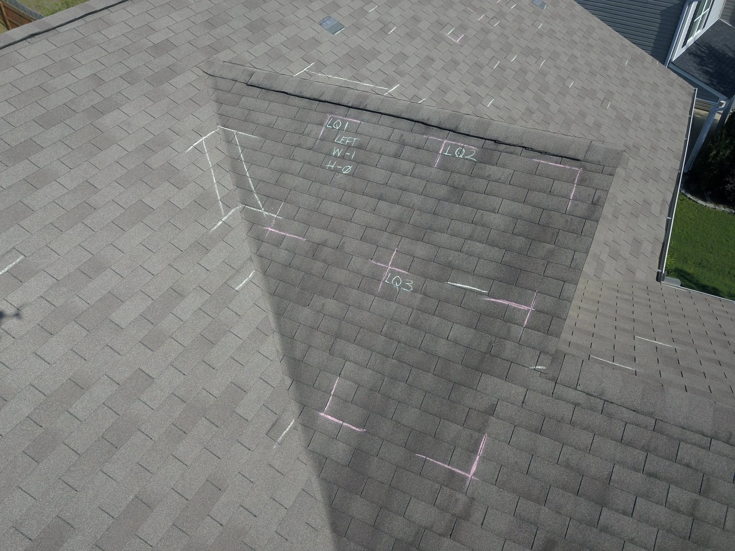 A rooftop with gray asphalt shingles marked with white and pink chalk markings for a construction or repair project.