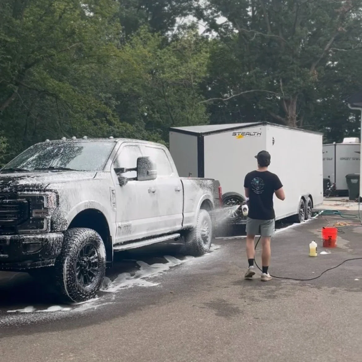 A man in a red and white striped shirt and shorts standing next to a boat on a trailer near a lake, with water and a dock in the background.