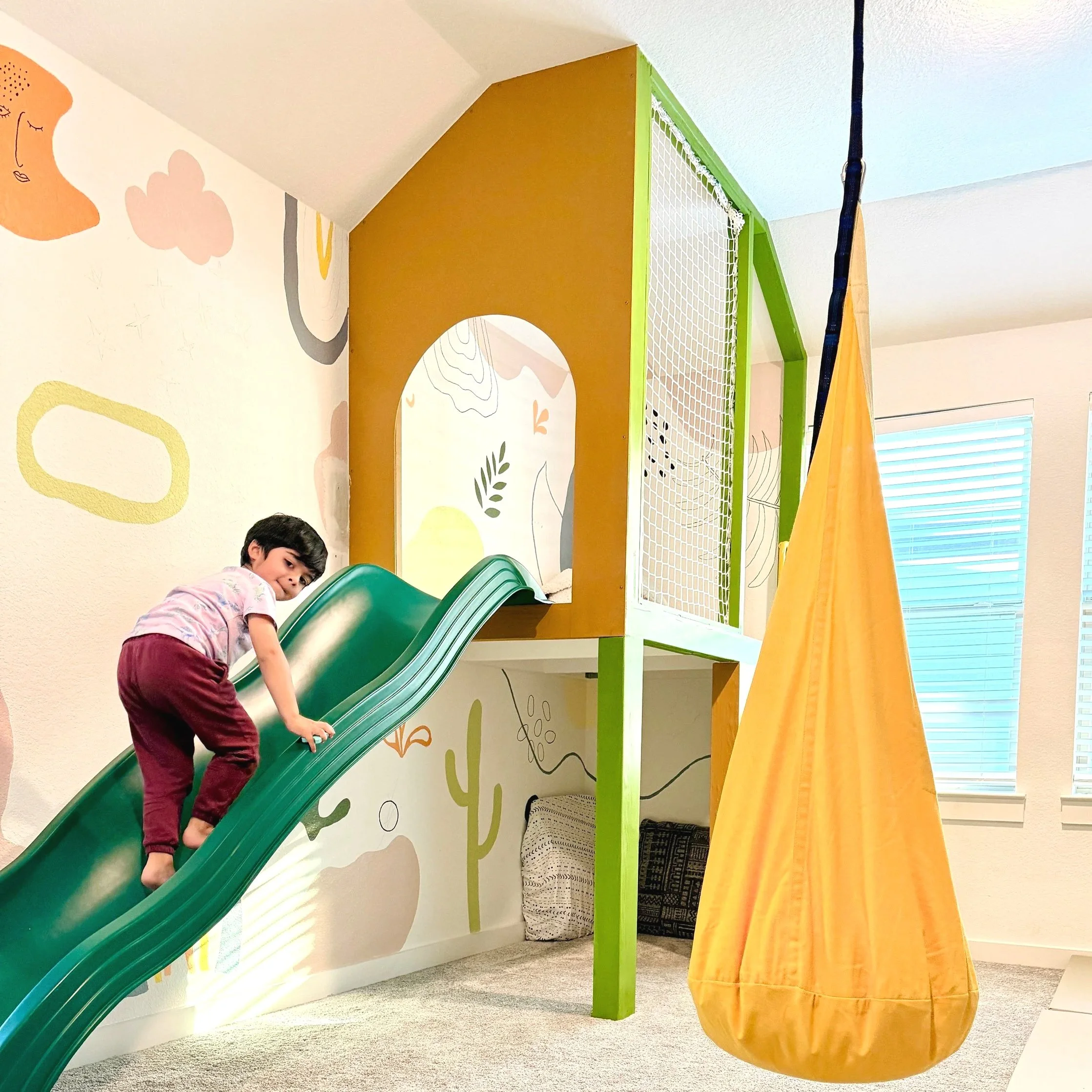 Happy little boy climbing up a green slide onto an indoor play platform