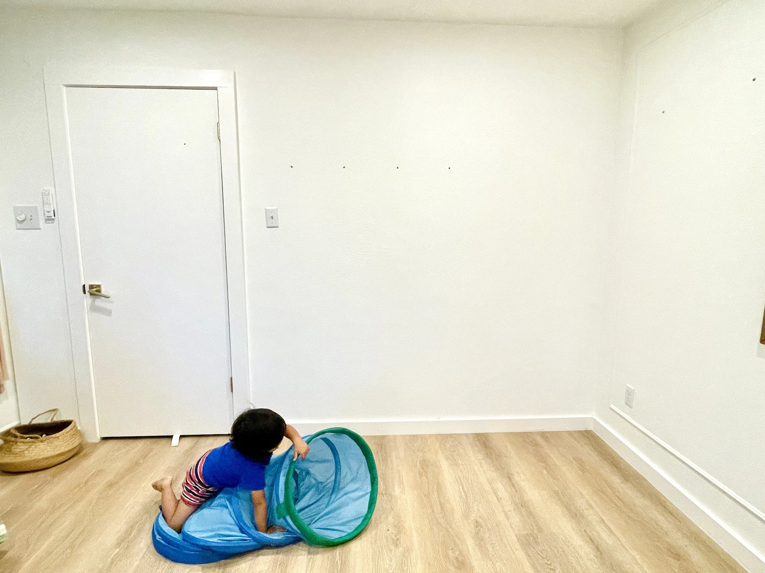 Bare white wall and a toddler playing in a tunnel