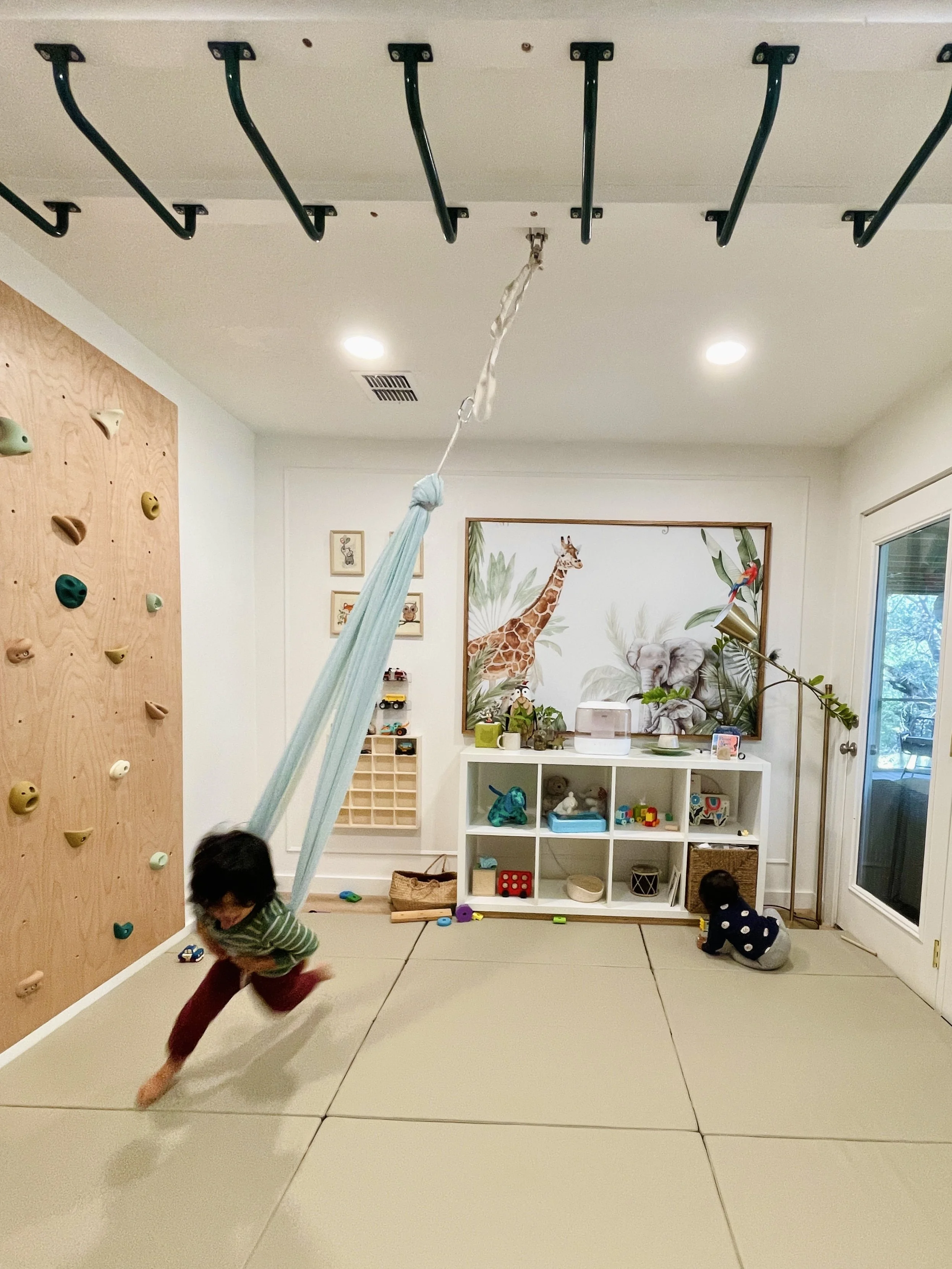 Toddler swinging while infant plays on mat