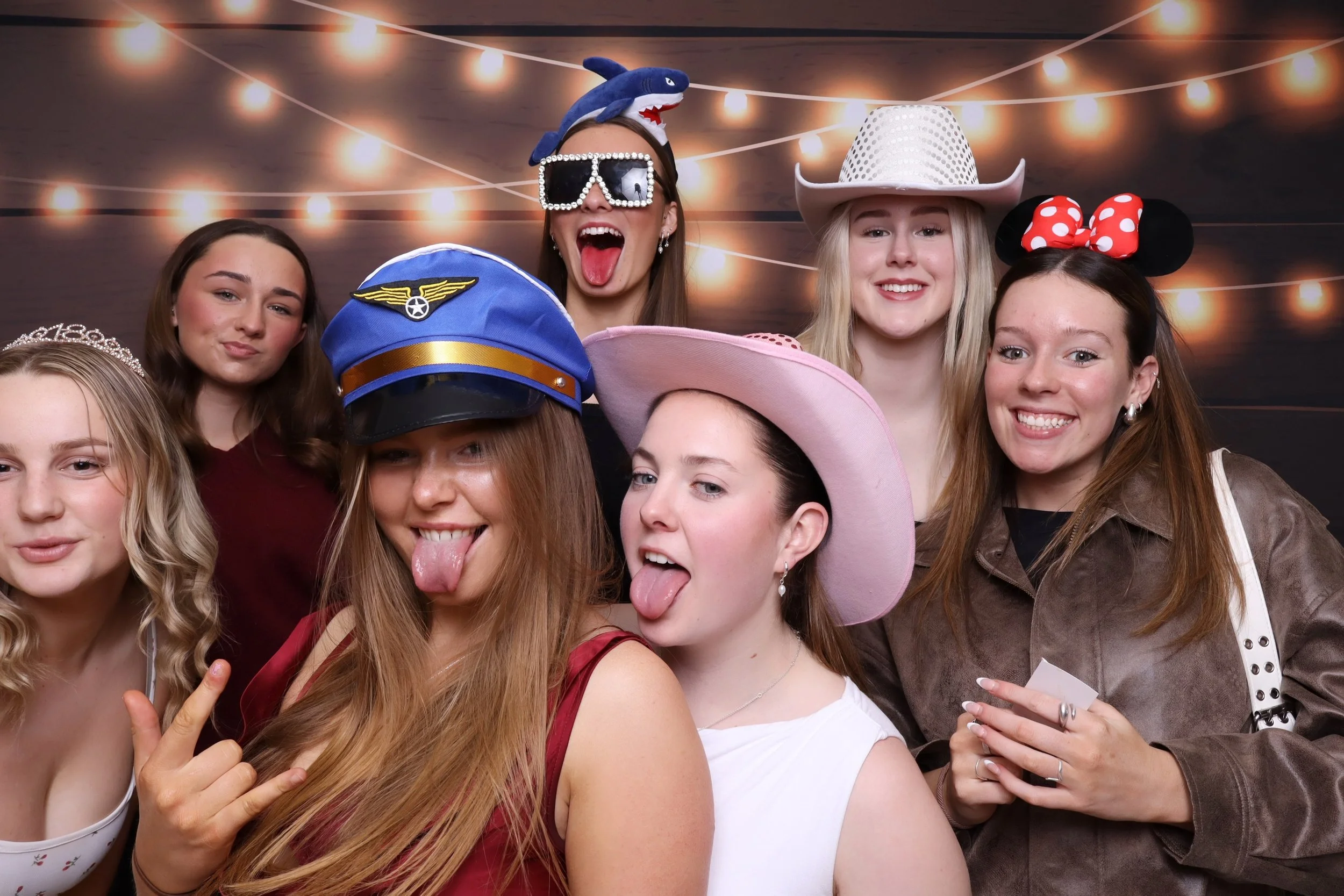 Group of young women celebrating at a party with fun hats and accessories, smiling and making playful gestures.