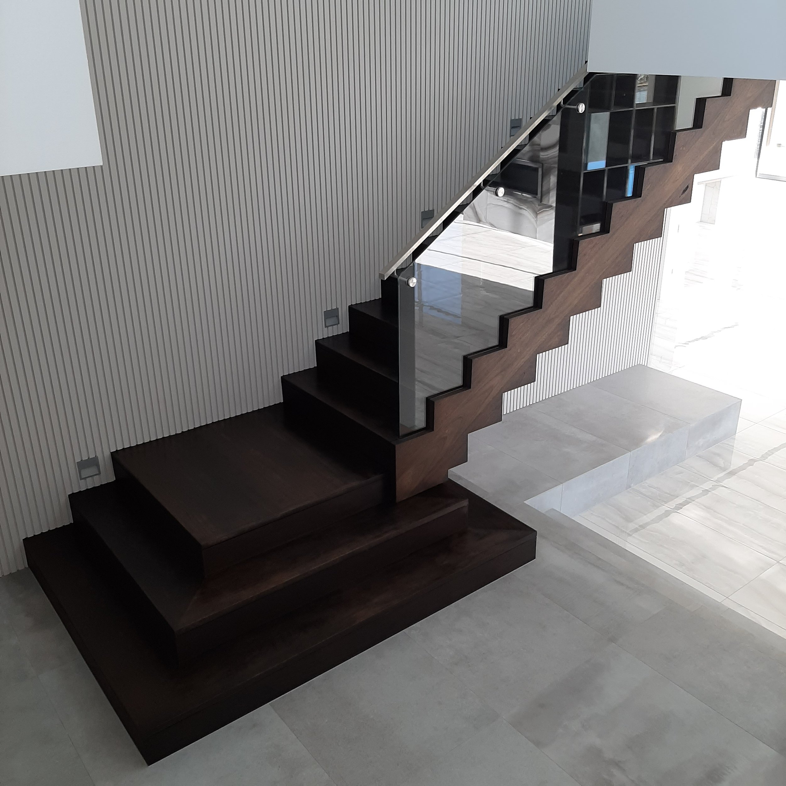 Modern staircase with dark wood steps, glass railing, and a textured wall in a contemporary interior space.