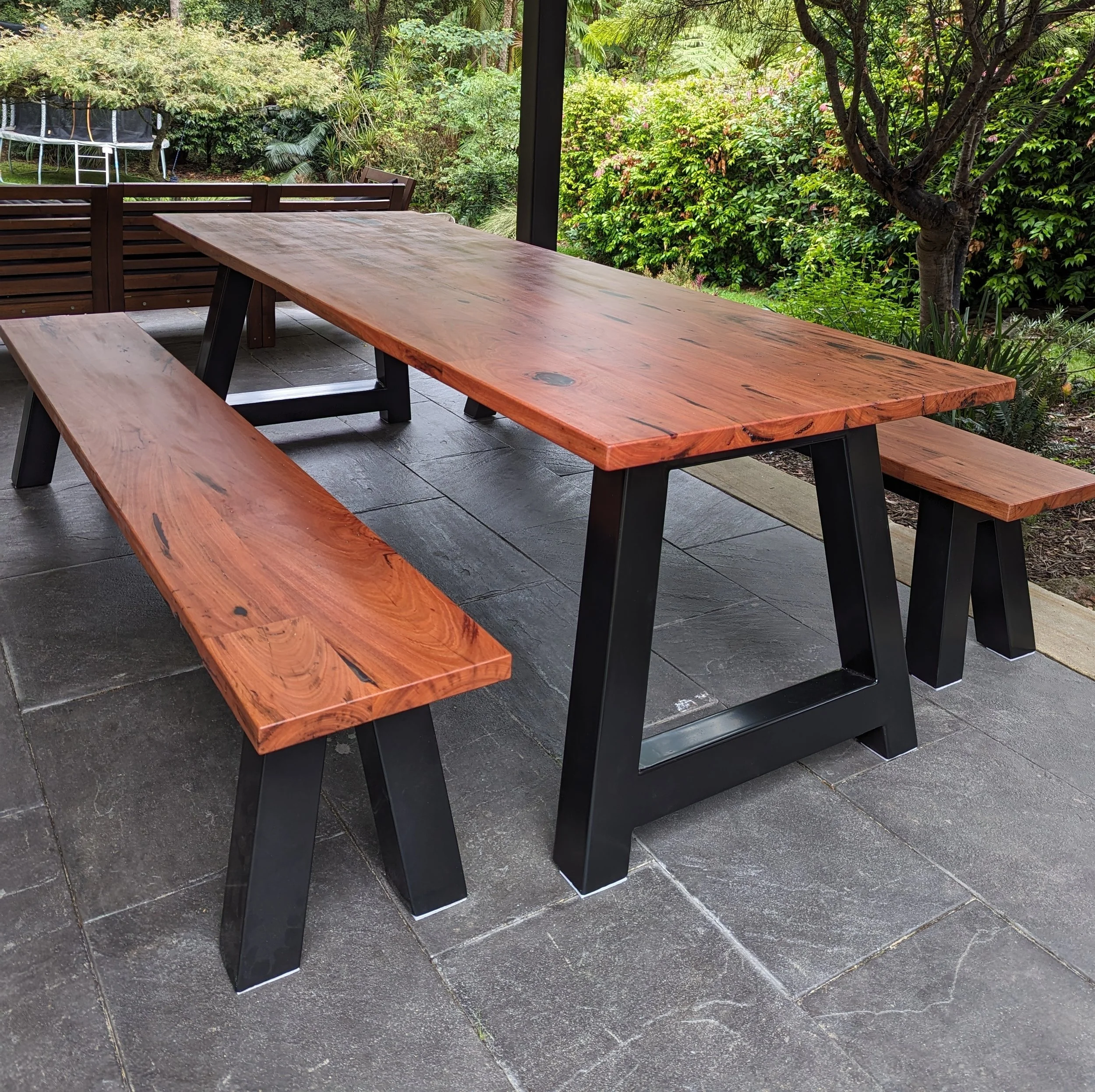 Wooden outdoor table with matching benches on a patio with a garden background.